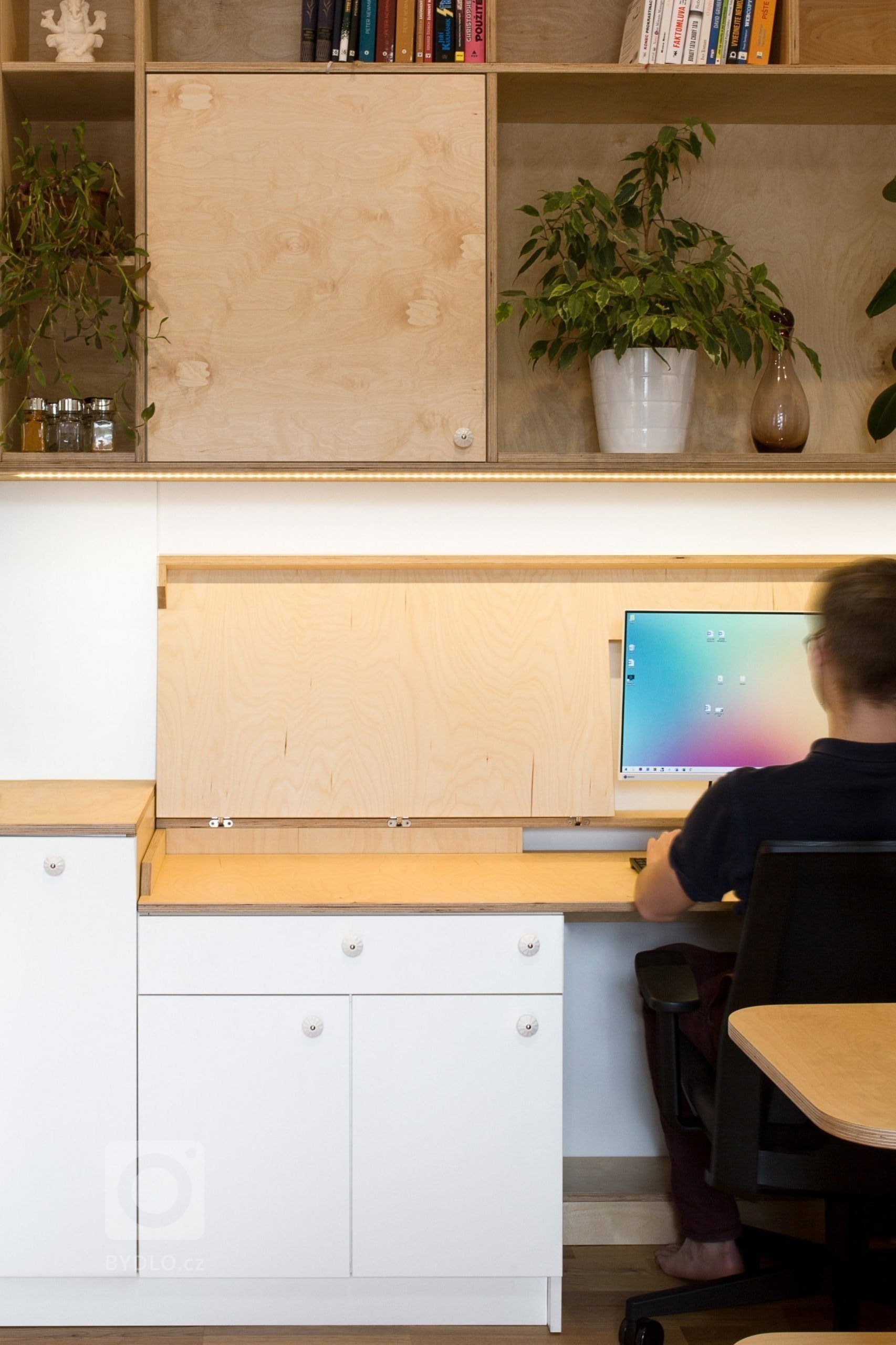 Při práci se deska pracovního stolu vyklopí, k dispozici je zde široký pracovní stůl. Úložné prostory pro kancelářské potřeby se nacházejí po stranách stolu, na stěna nad hlavou pracujícího a za zády v boční části sedací soupravy