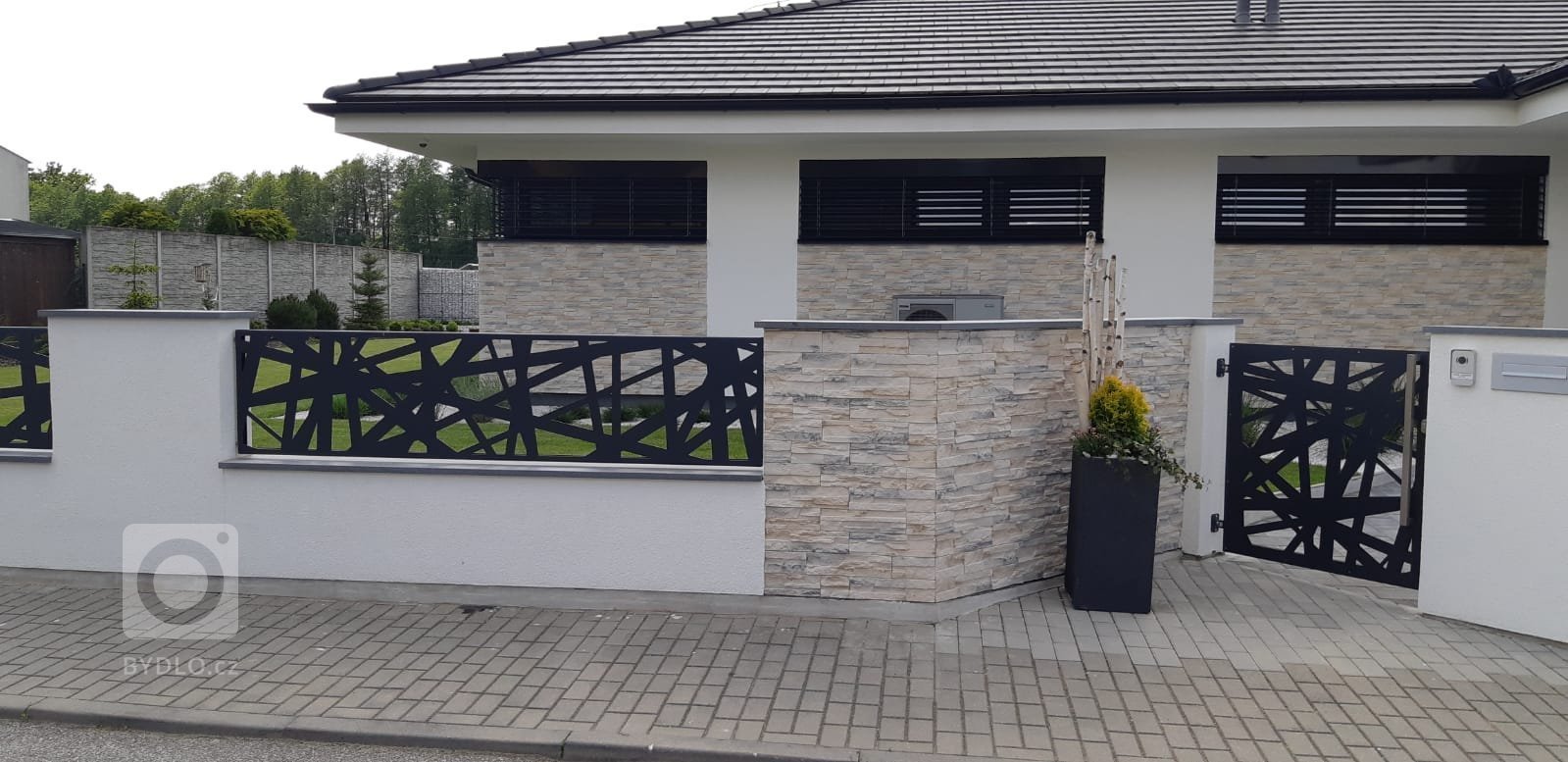 Realizované oplocení nového rodinného domu. Výška plotových dílců koresponduje se šířkou oken domu v pozadí. Moderní design však strhává pozornost více na…