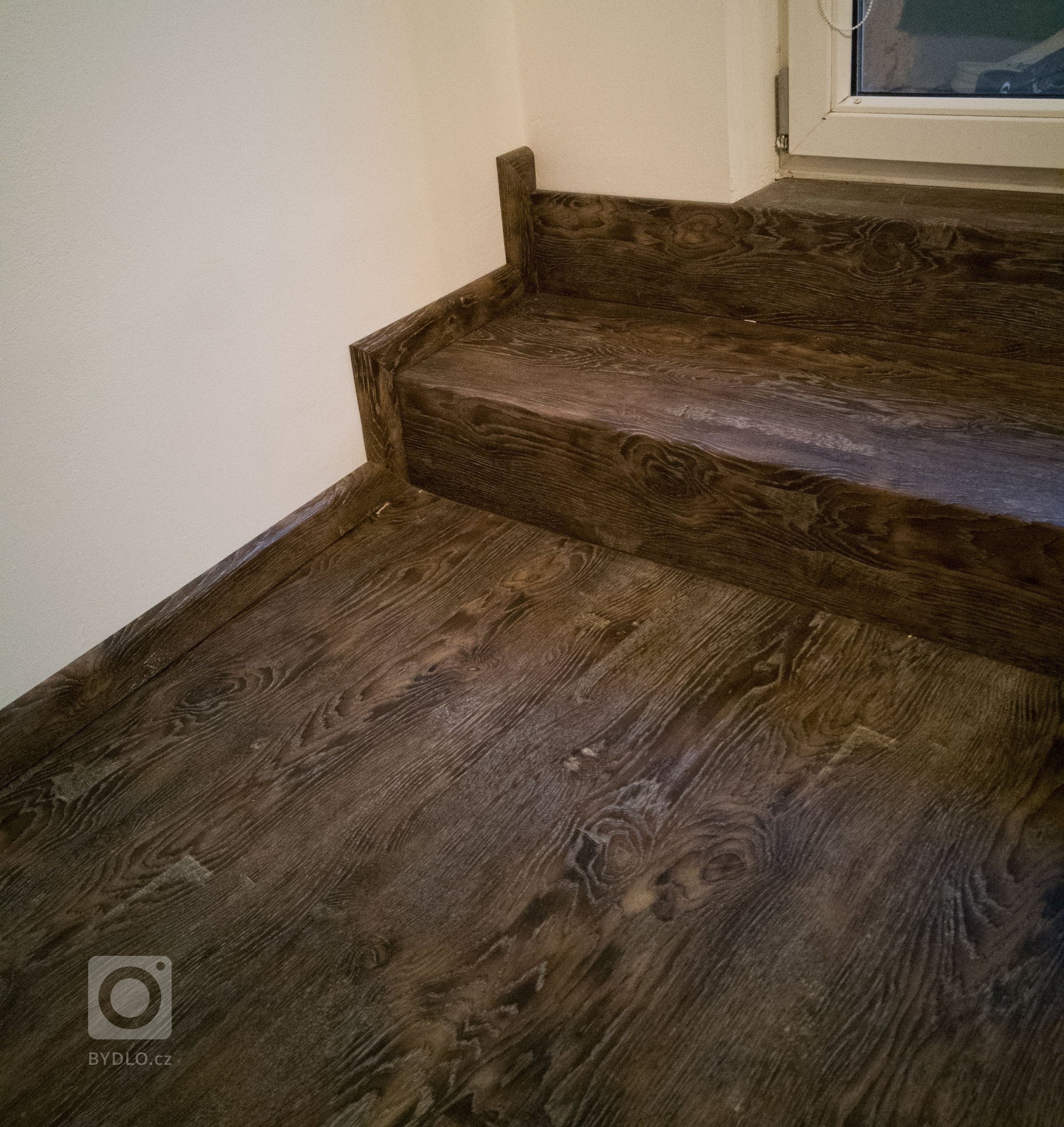 Původní obklad schodů na terasu z keramické dlažby byl nahrazen schody z vinylové podlahy ve stejném dekoru jako ostatní podlaha. Schodová hrana je řešena bez použití kovové schodové lišty.