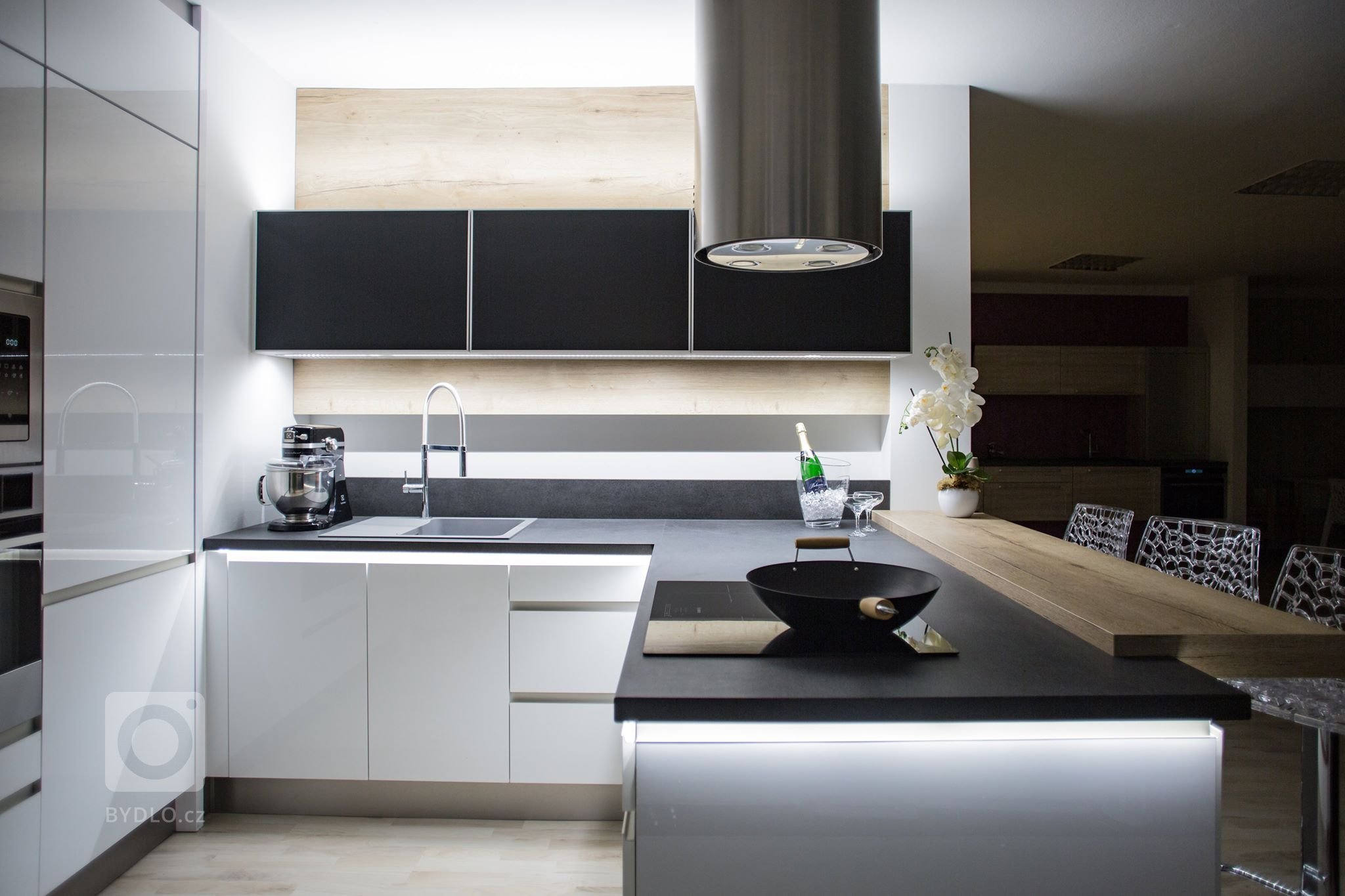 Chytré Kuchyně - bílý lesk s výraznou černou pracovní deskou a nadčasovým dřevodekorem s neparavidelnou kresbou.&nbsp;
