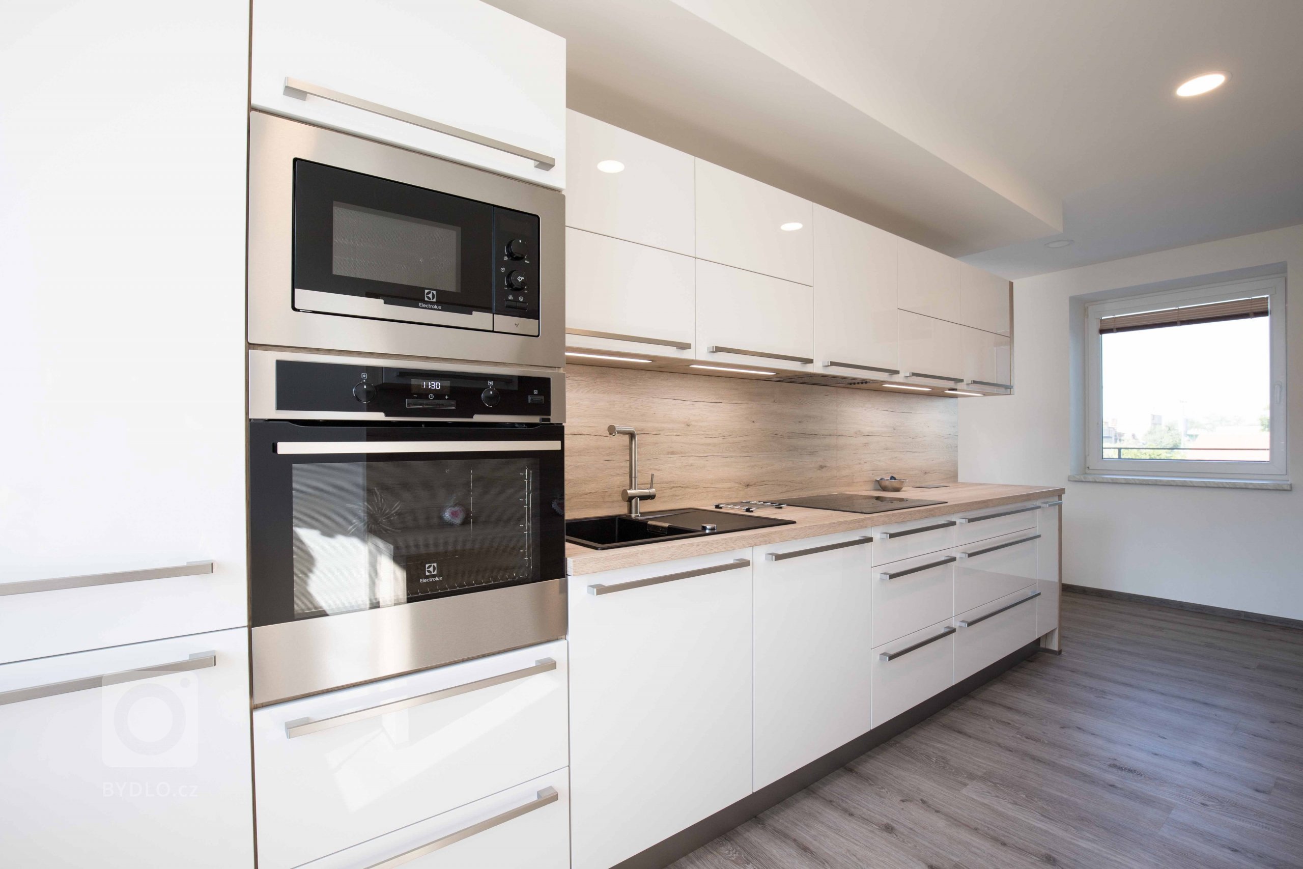 Dřevo v kombinaci s bílou je vždy dobrý nápad. Nechybí vestavěné spotřebiče a praktické výsuvné systémy.
