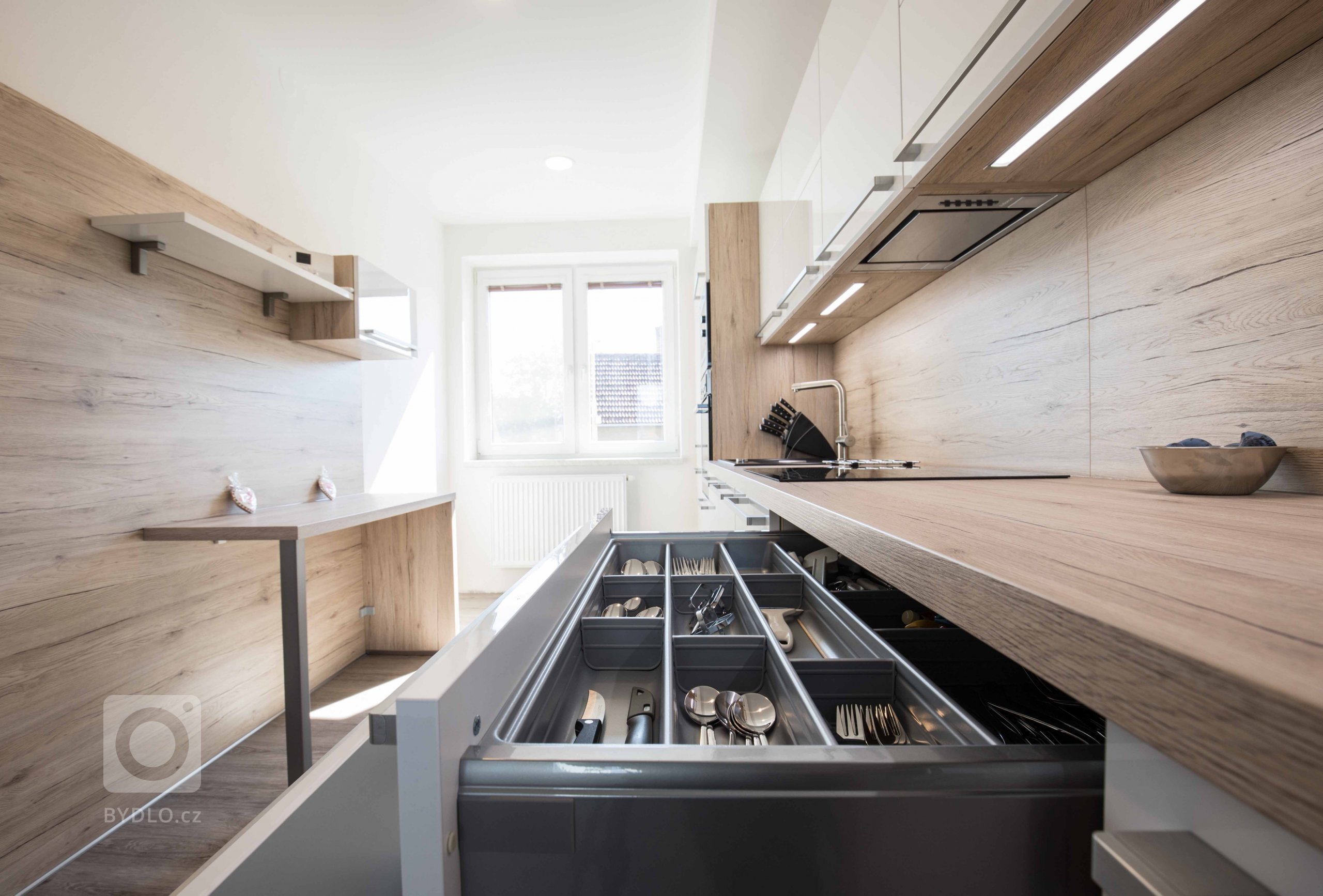 Dřevo v kombinaci s bílou je vždy dobrý nápad. Nechybí vestavěné spotřebiče a praktické výsuvné systémy.
