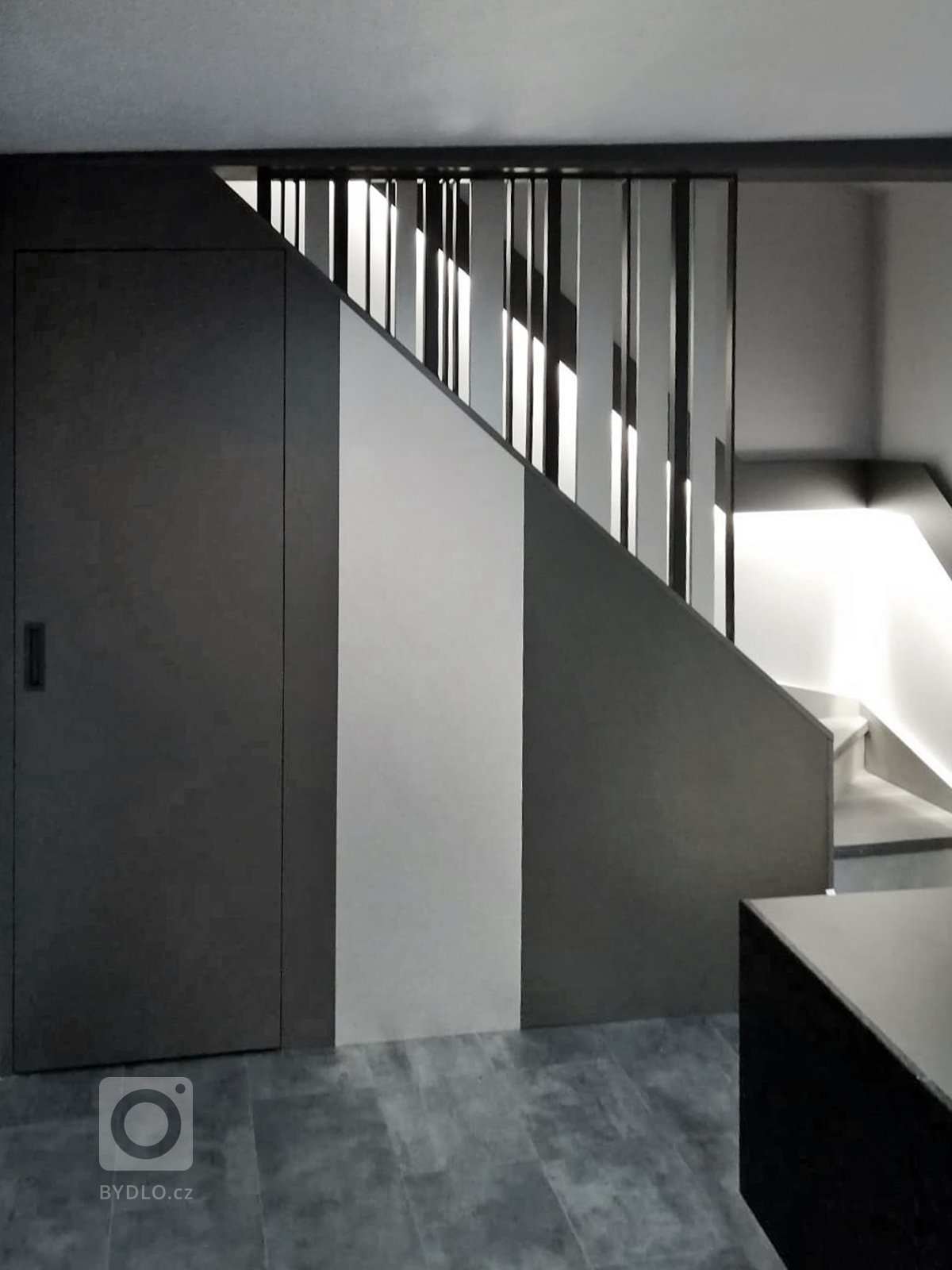 Nový stav prostoru pod schodištěm se zabudovaným prostorem pro vestavné WC. Použito metalické LTD od firmy Pflaiderer v kombinaci se stříbrným Homapalem. 