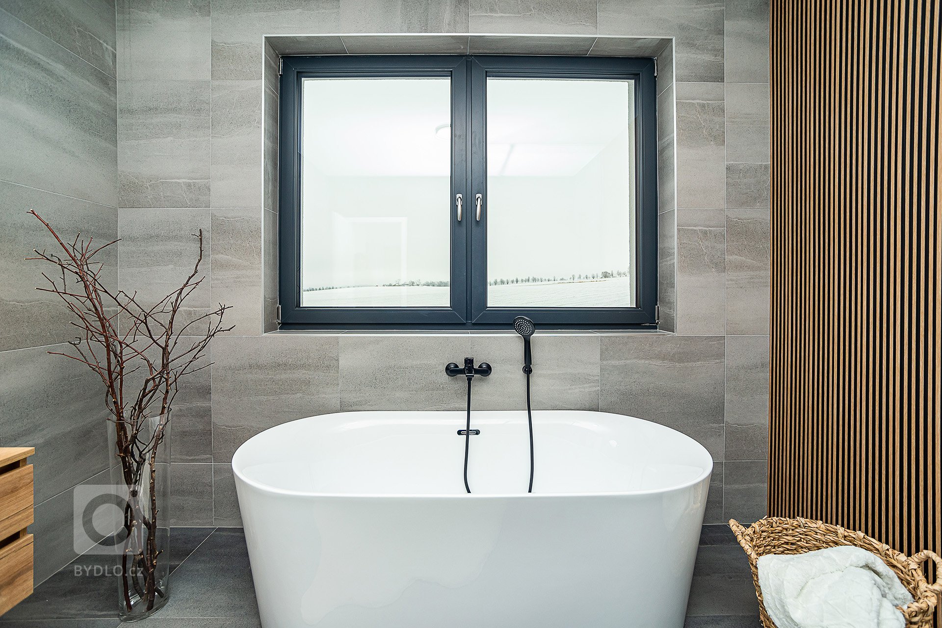 Interiér rodinného domu byl navržen v kombinaci olejovaného dubu, laminátu v odstínu taupe,&nbsp;černého lakovaného kovu a šedých odstínech velkoformátové…