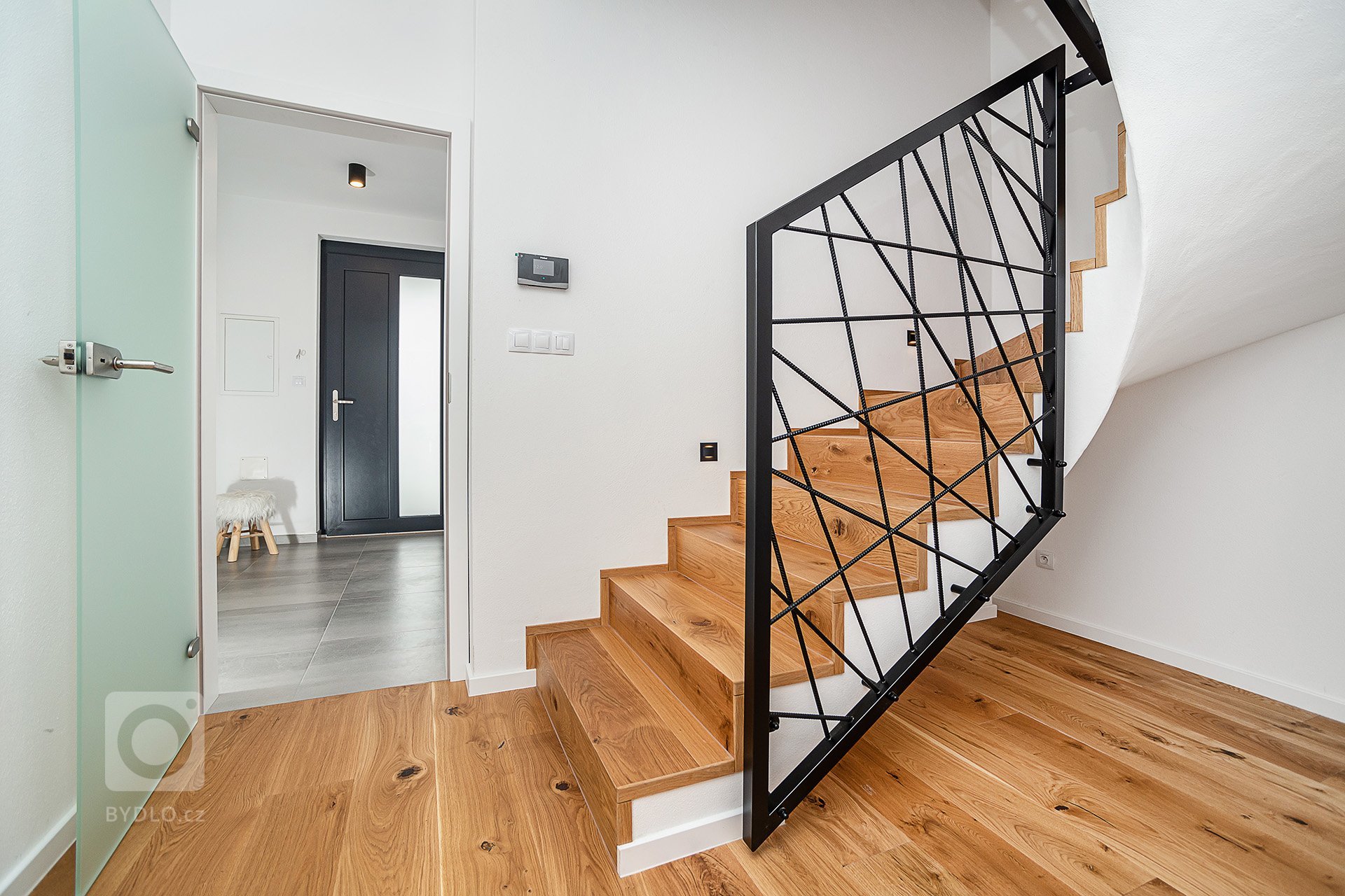 Interiér rodinného domu byl navržen v kombinaci olejovaného dubu, laminátu v odstínu taupe,&nbsp;černého lakovaného kovu a šedých odstínech velkoformátové…