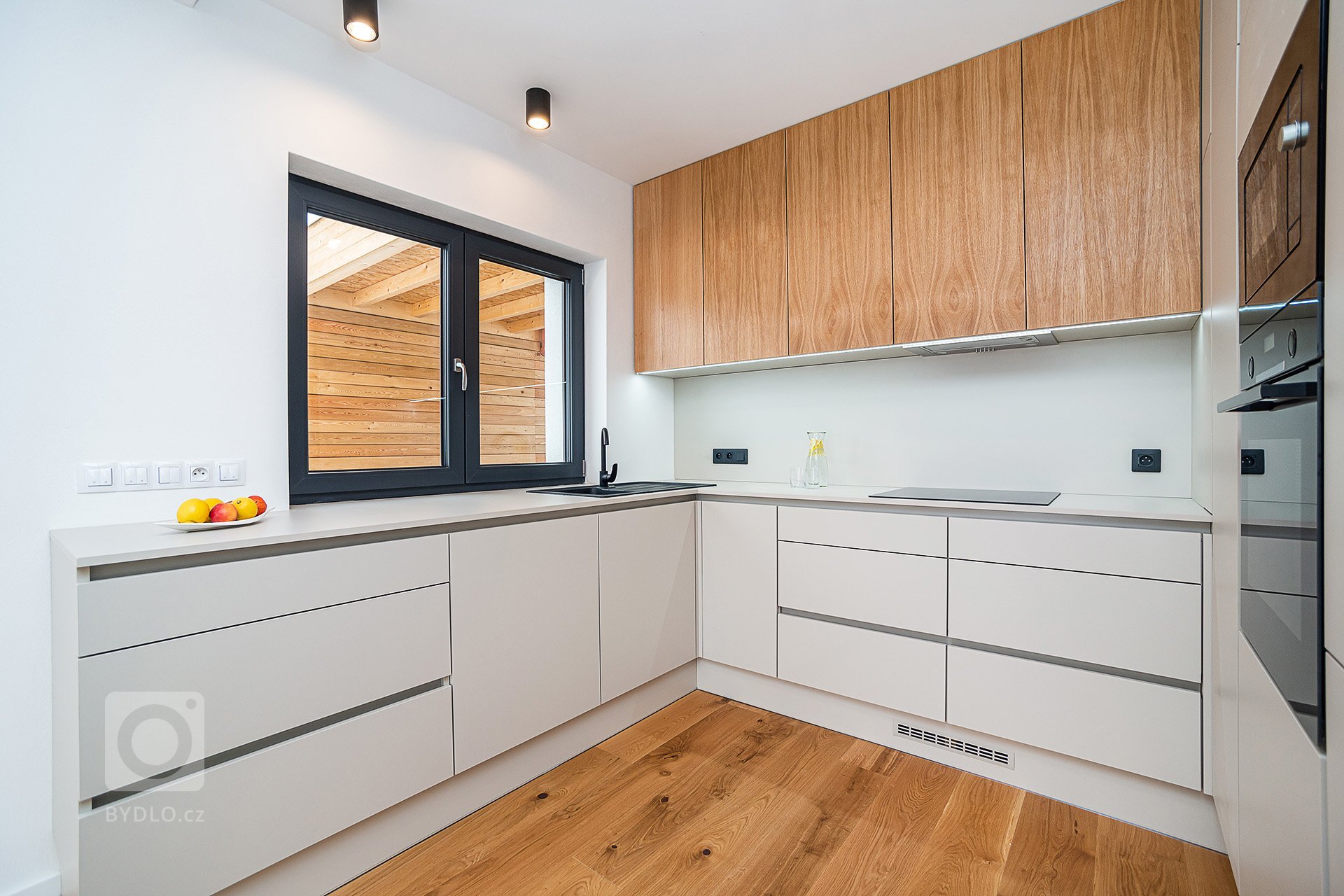 Interiér rodinného domu byl navržen v kombinaci olejovaného dubu, laminátu v odstínu taupe,&nbsp;černého lakovaného kovu a šedých odstínech velkoformátové…