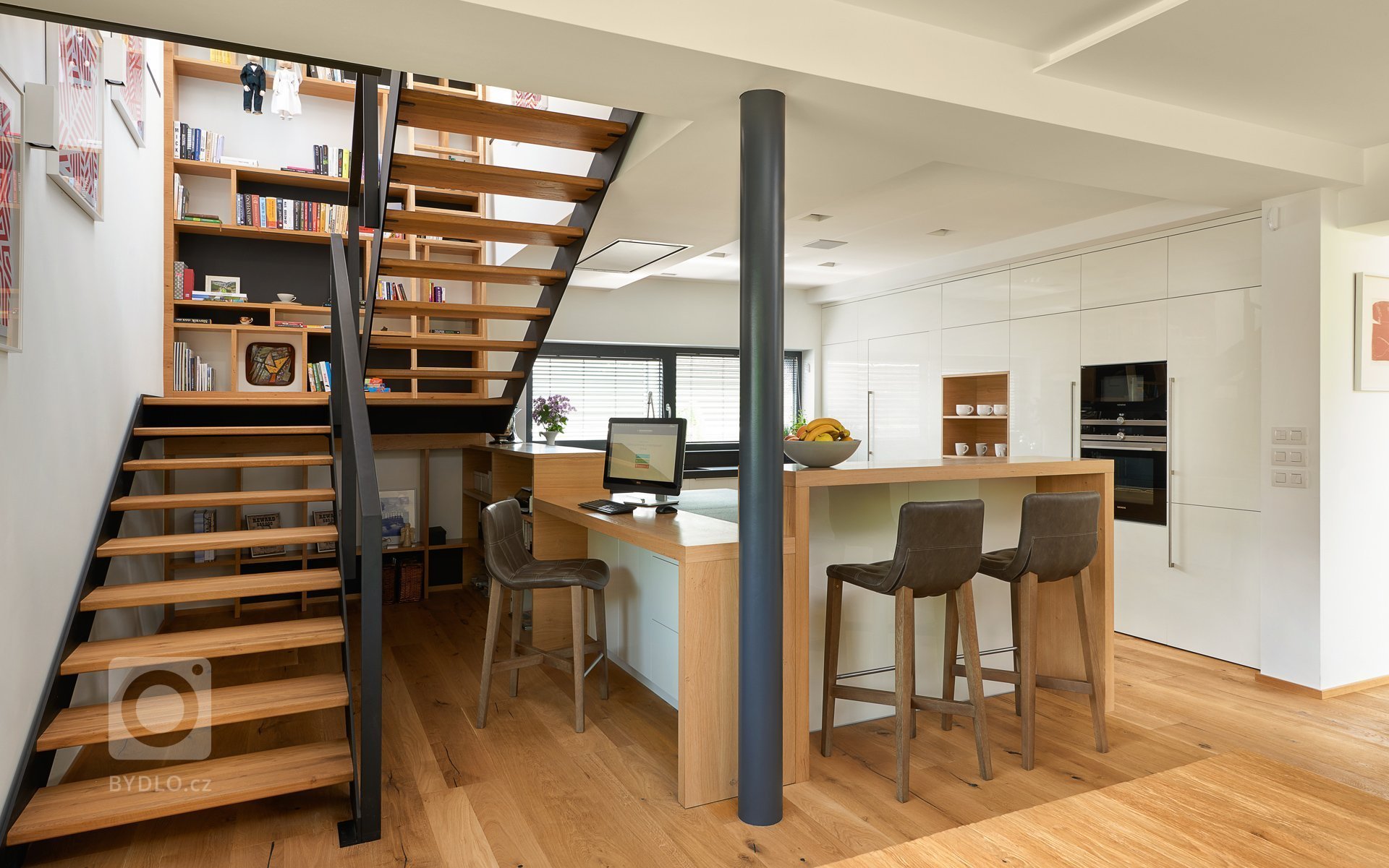 Interiér, kde se prolíná dýha dub rustikální přírodní spolu s bílým lakem ve vysokém lesku. Kuchyně získala v tomto prostorném domě místo při schodišti, které…