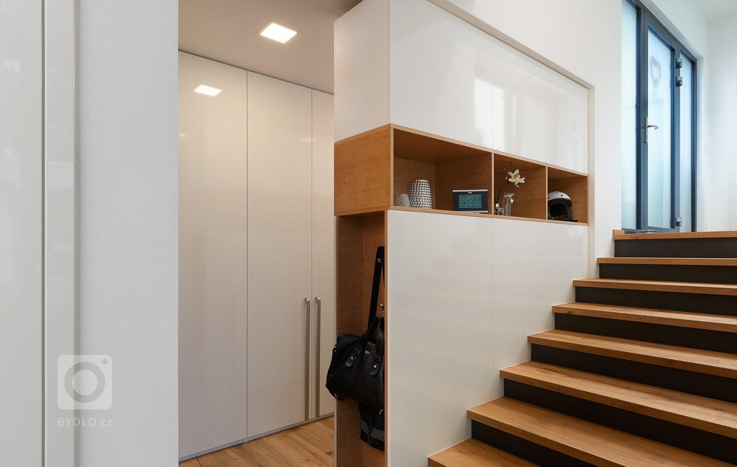 Interiér, kde se prolíná dýha dub rustikální přírodní spolu s bílým lakem ve vysokém lesku. Kuchyně získala v tomto prostorném domě místo při schodišti, které…