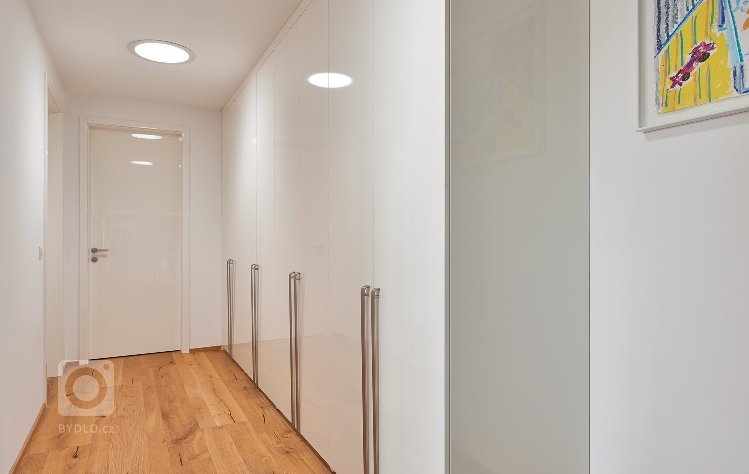 Interiér, kde se prolíná dýha dub rustikální přírodní spolu s bílým lakem ve vysokém lesku. Kuchyně získala v tomto prostorném domě místo při schodišti, které…