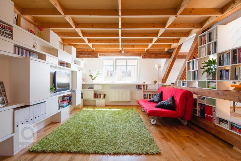 Knihovna je vložena do trámoví podkrovního bytu, odděluje prostor obývacího pokoje a kuchyně, ale zároveň ponechává vizuální kontakt. Ortogonální rastr otvorů…