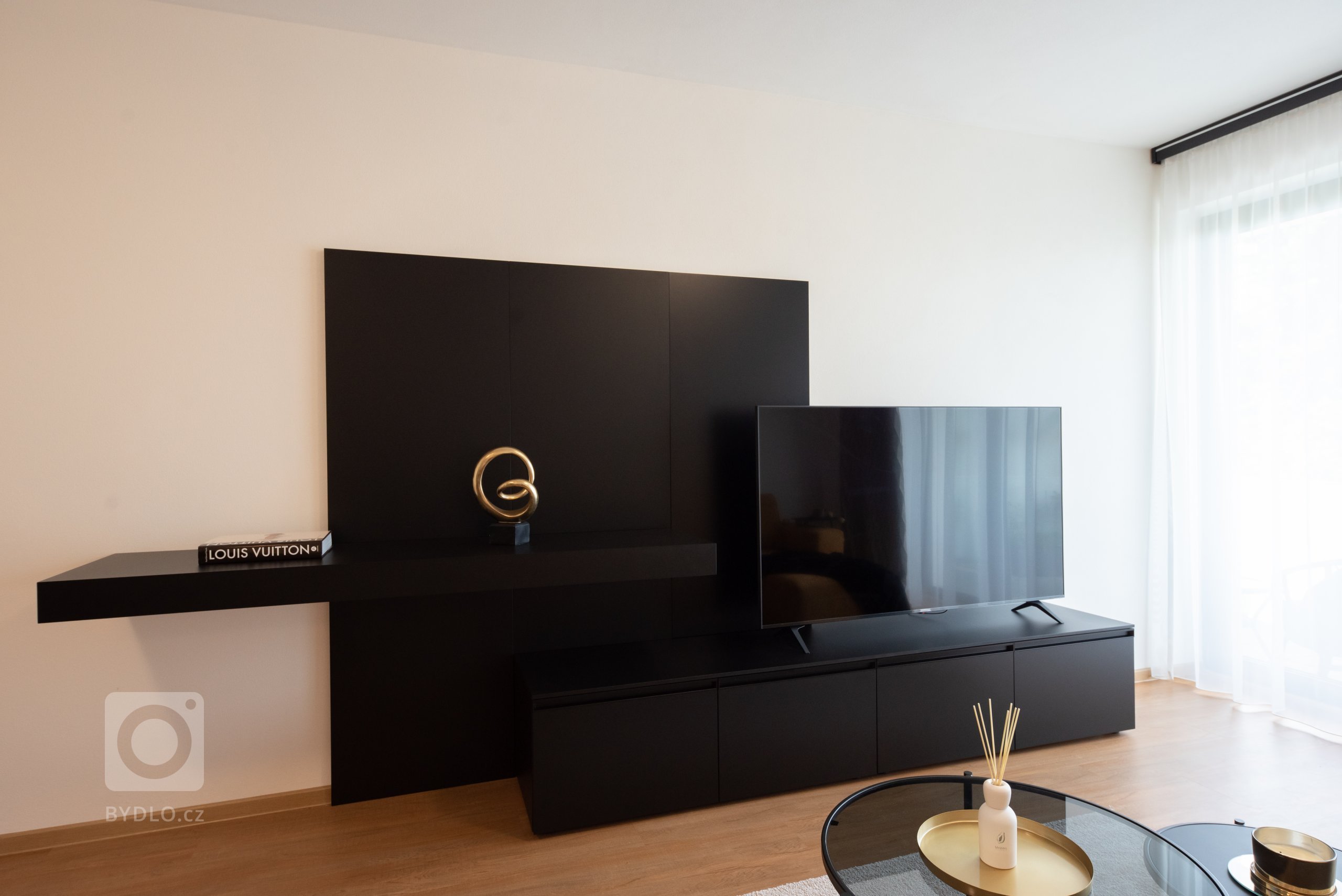 Realizace moderního obývacího pokoje a ložnice v glamour stylu.&nbsp;

Sedací souprava je z kolekce MONO s výsuvnými sedáky, obývací stěna je v černém matném…