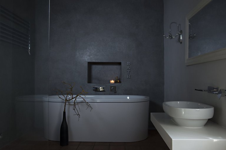 Koupelna s marockým štukem, prostornou vanou a vlevo sprchovým koutem odděleným skleněnou stěnou.