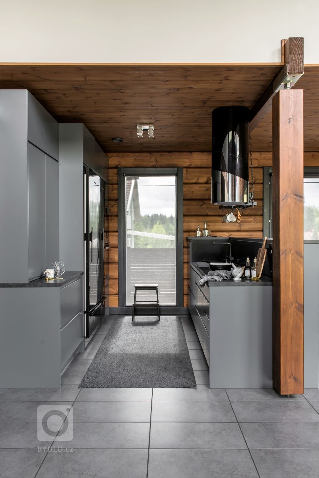 Kouřově šedé dlaždice ladí s kuchyňskou linkou rovněž šedé barvy. Černá barva lednice a mrazáku dodávají interiéru jiskru. 