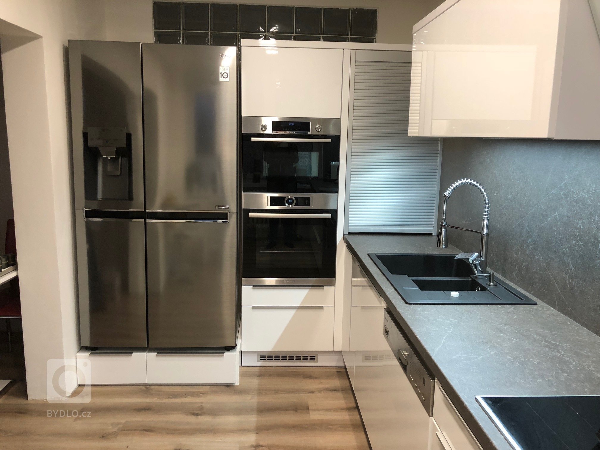 Kuchyňká linka v bílém vysokém lesku s grafosklem, osazená spotřebiči Bosch a doplněná příruční&nbsp;stolovou deskou zabudovanou do skříňkové sestavy…