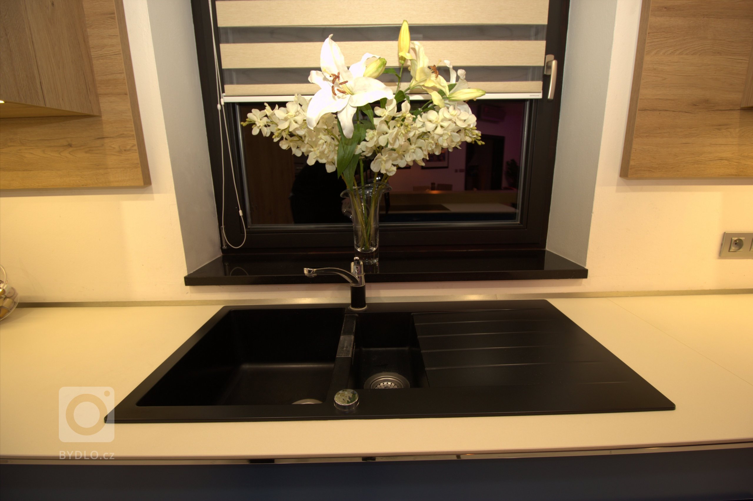 Tmavý granitový dřez je dominantou pracovní desky z umělého kamene.
