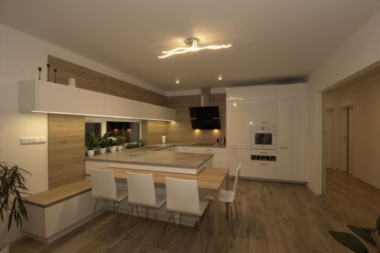 Vize klientky byla jasná, kuchyň s&nbsp;vysokým dřevěným obkladem a vybíhající horní bílá skříňka.

Kuchyně je ve tvaru U a na ní navazující stůl. Stůl je…