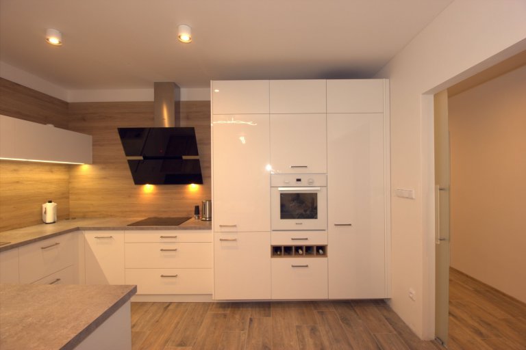 Bílá kuchyň doplněná přírodním dubem.