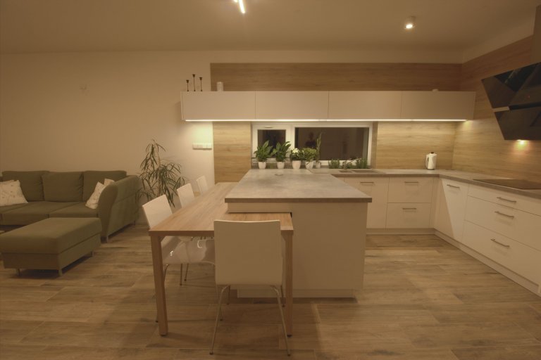 Vize klientky byla jasná, kuchyň s&nbsp;vysokým dřevěným obkladem a vybíhající horní bílá skříňka.

Kuchyně je ve tvaru U a na ní navazující stůl. Stůl je…