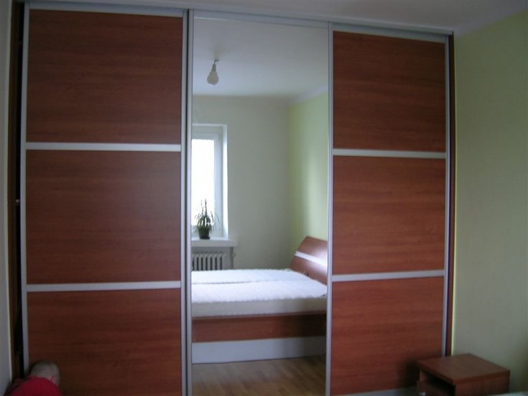 Ložnice s postelí s úložným prostorem, nočními stolky a vestavěnou skříní.
