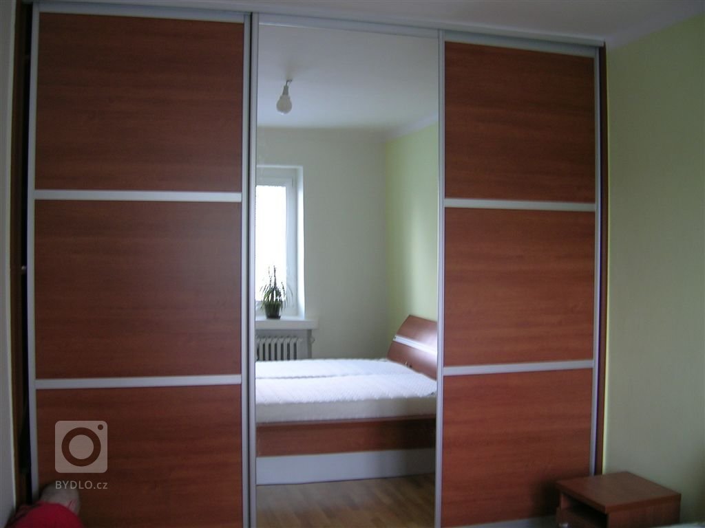 Ložnice s postelí s úložným prostorem, nočními stolky a vestavěnou skříní.
