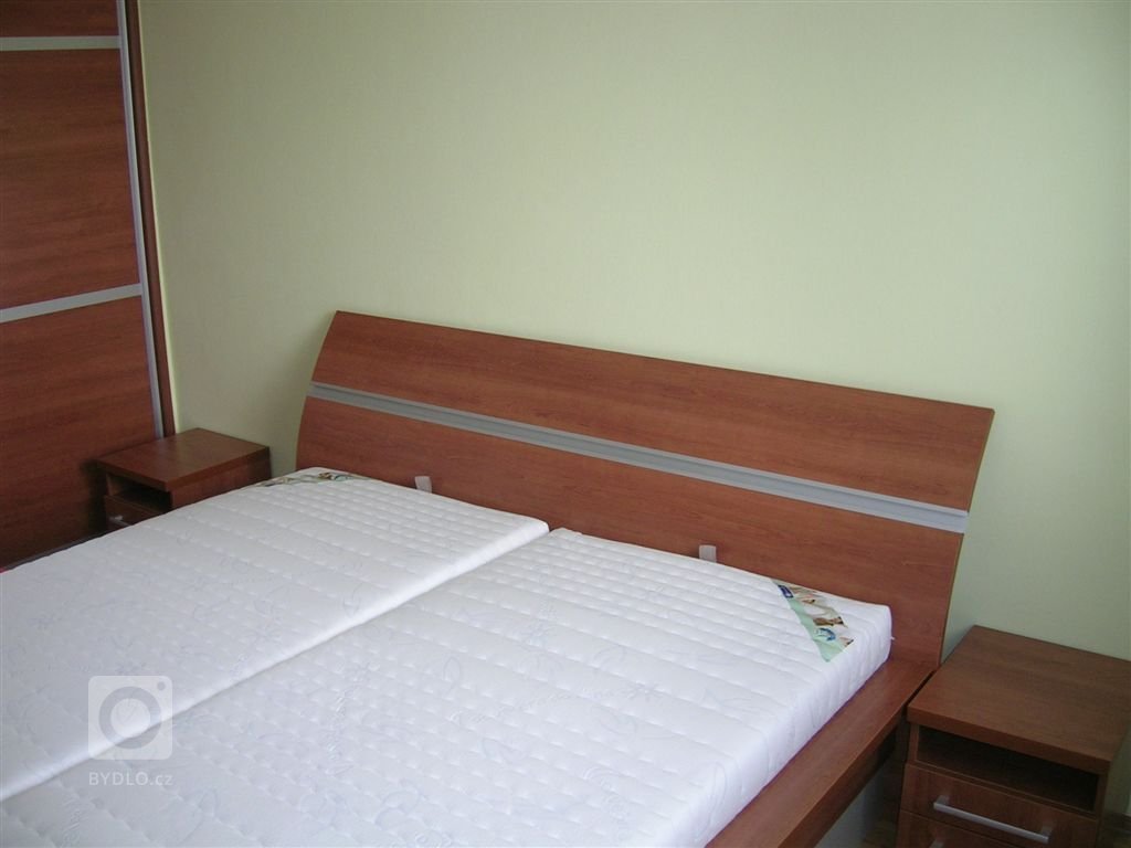 Ložnice s postelí s úložným prostorem, nočními stolky a vestavěnou skříní.
