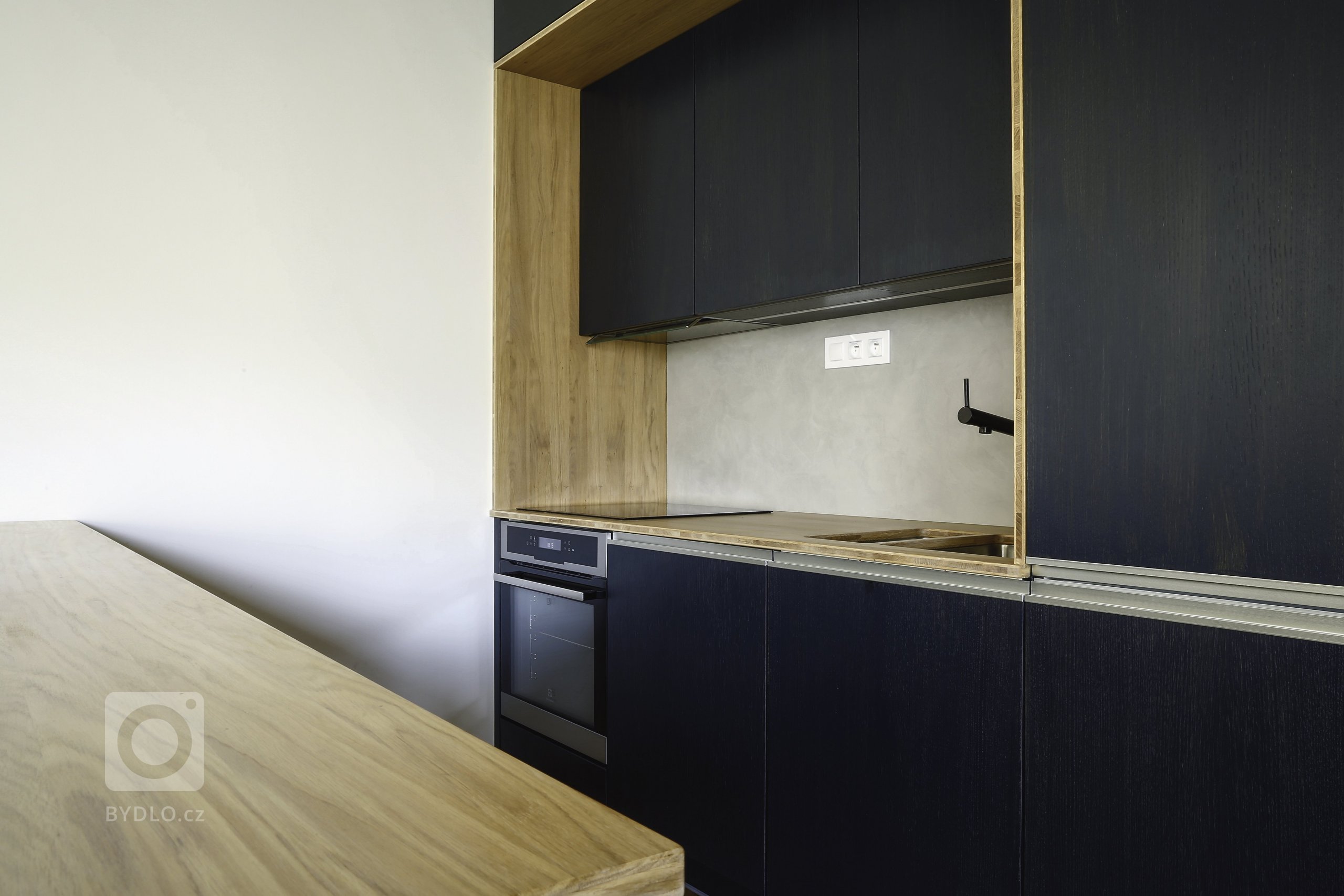 Odvážná kuchyně v novostavbě, kdy je tmavá barva zjemněná dubovou bio deskou a kresba dřeva pod dýhovaným mořeným dvířkem krásně prostupuje a vytváří zajímavý…