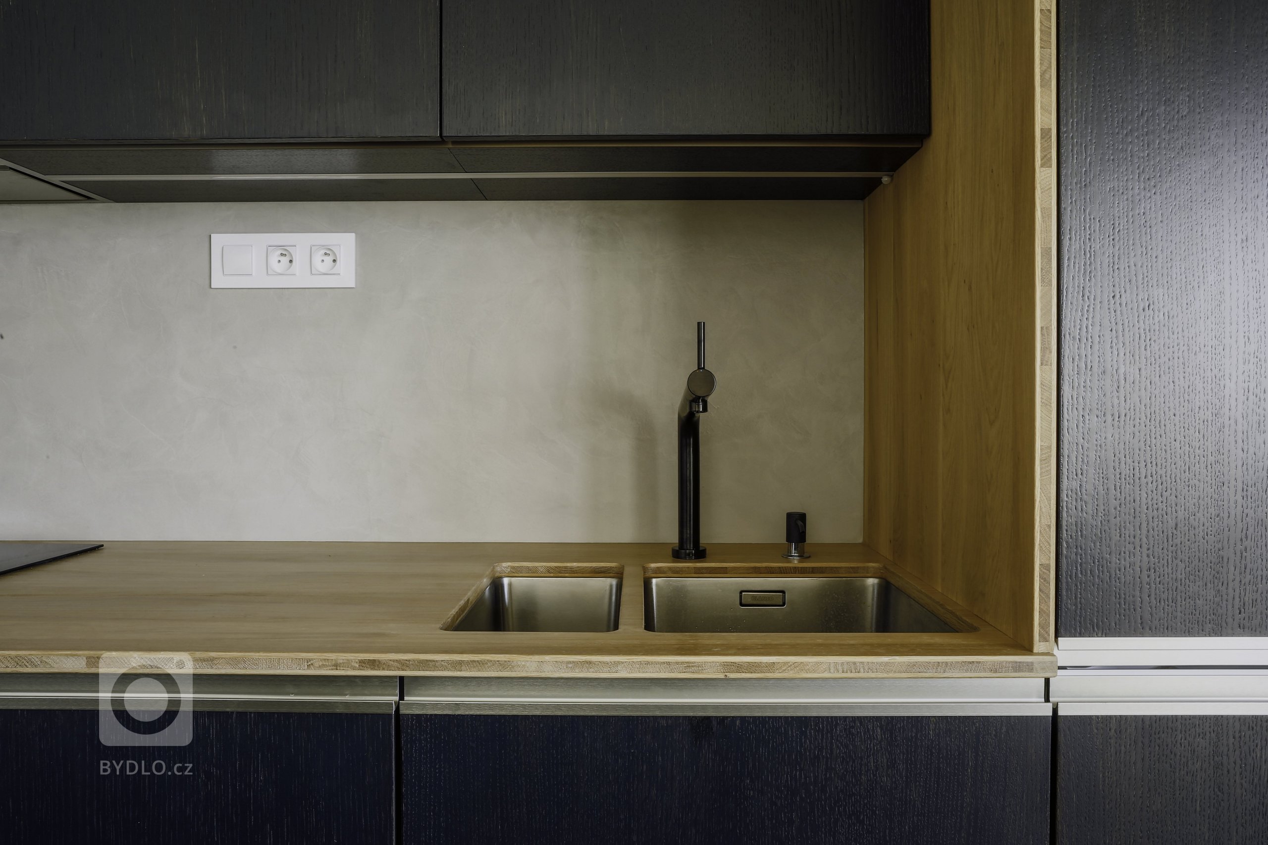 Odvážná kuchyně v novostavbě, kdy je tmavá barva zjemněná dubovou bio deskou a kresba dřeva pod dýhovaným mořeným dvířkem krásně prostupuje a vytváří zajímavý…
