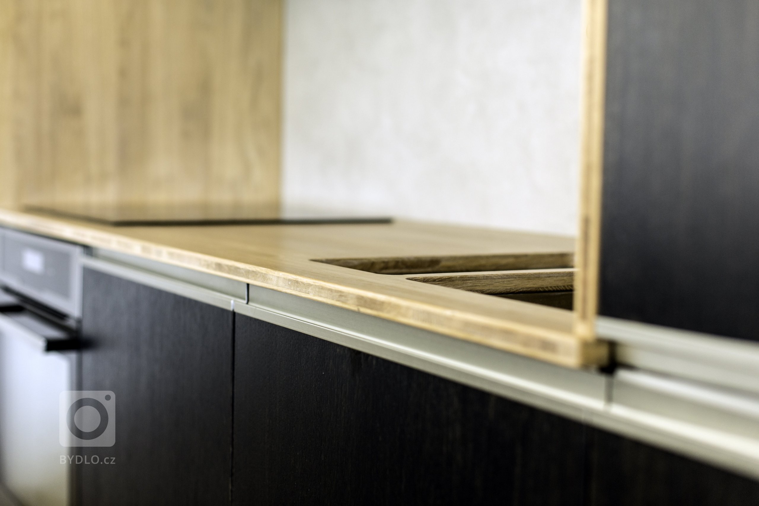 Odvážná kuchyně v novostavbě, kdy je tmavá barva zjemněná dubovou bio deskou a kresba dřeva pod dýhovaným mořeným dvířkem krásně prostupuje a vytváří zajímavý…