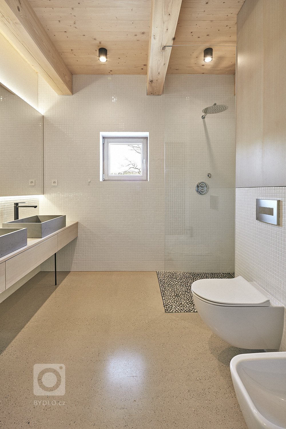 Pozemek leží na hraně svahu v&nbsp;centru malé obce na Vysočině. Na půdorysné stopě bývalého statku vznikl dům a stodola. Dům má podél jihozápadní fasády kryté…