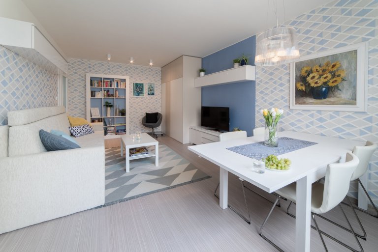 Původní velmi tmavý obývací pokoj se novým bílo-modro-béžovým laděním proměnil v příjemně světlý, svěží prostor. Výrazné tapety a koberec s pastelovými vzory…