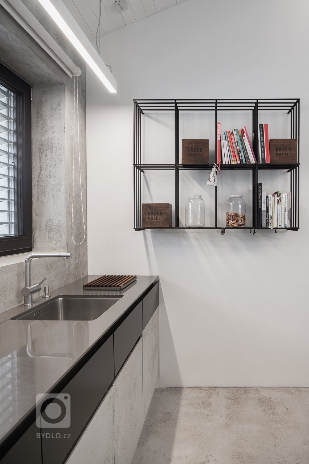 Policová sestava z ocelových prutů je elegantním protikladem k masivní železobetonové kuchyni. 