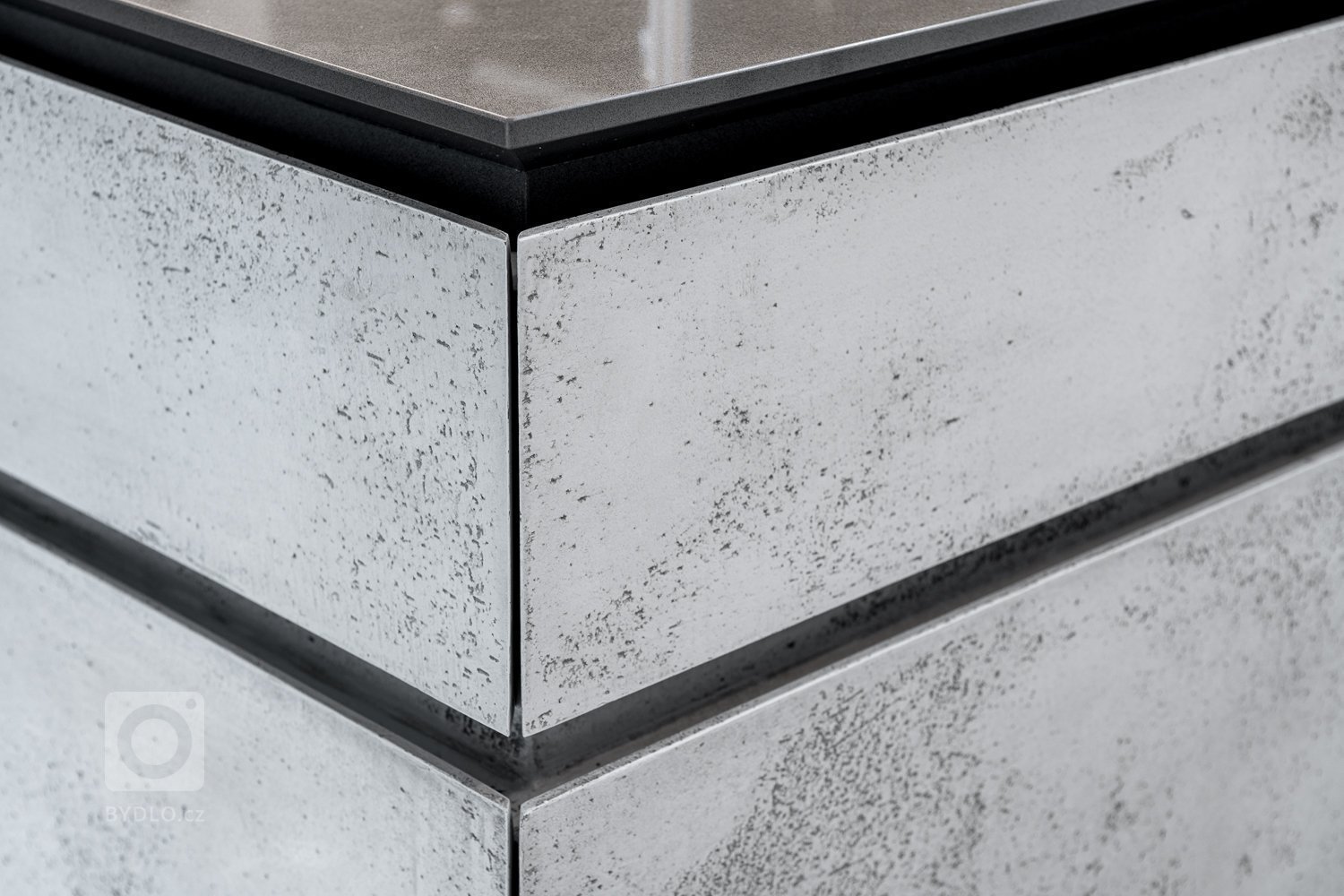 Subtilní pracovní deska je z umělého kamene. Pro zachování čistého designu byla použita kombinace bezúchytkového systému tipon s tichým dojezdem a elektrický systém “servo-drive”. 