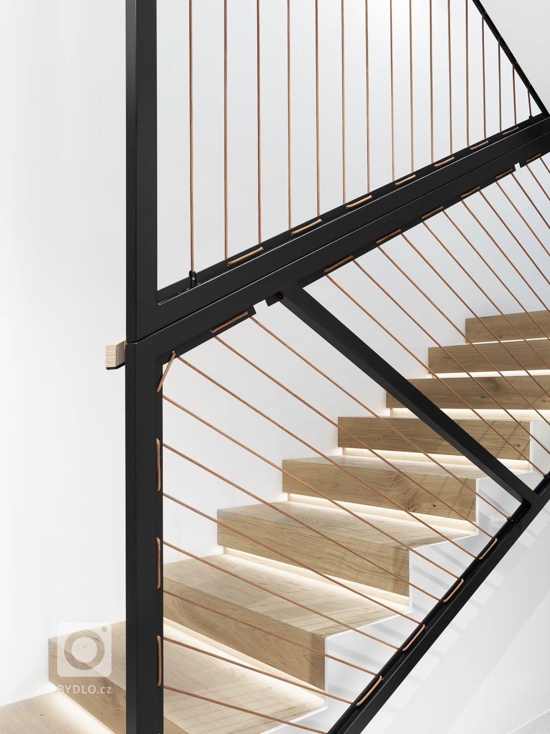 Ocelová černá konstrukce zábradlí zajišťuje bezpečnou chůzi po schodech, a to díky výpletu z kožených lanek.