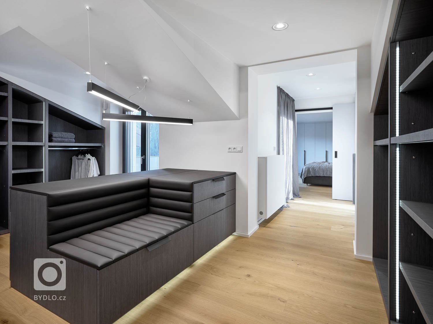 Uprostřed šatny se nachází podsvícený ostrůvek, který obsahuje úložné prostory a zároveň slouží jako lavice. 