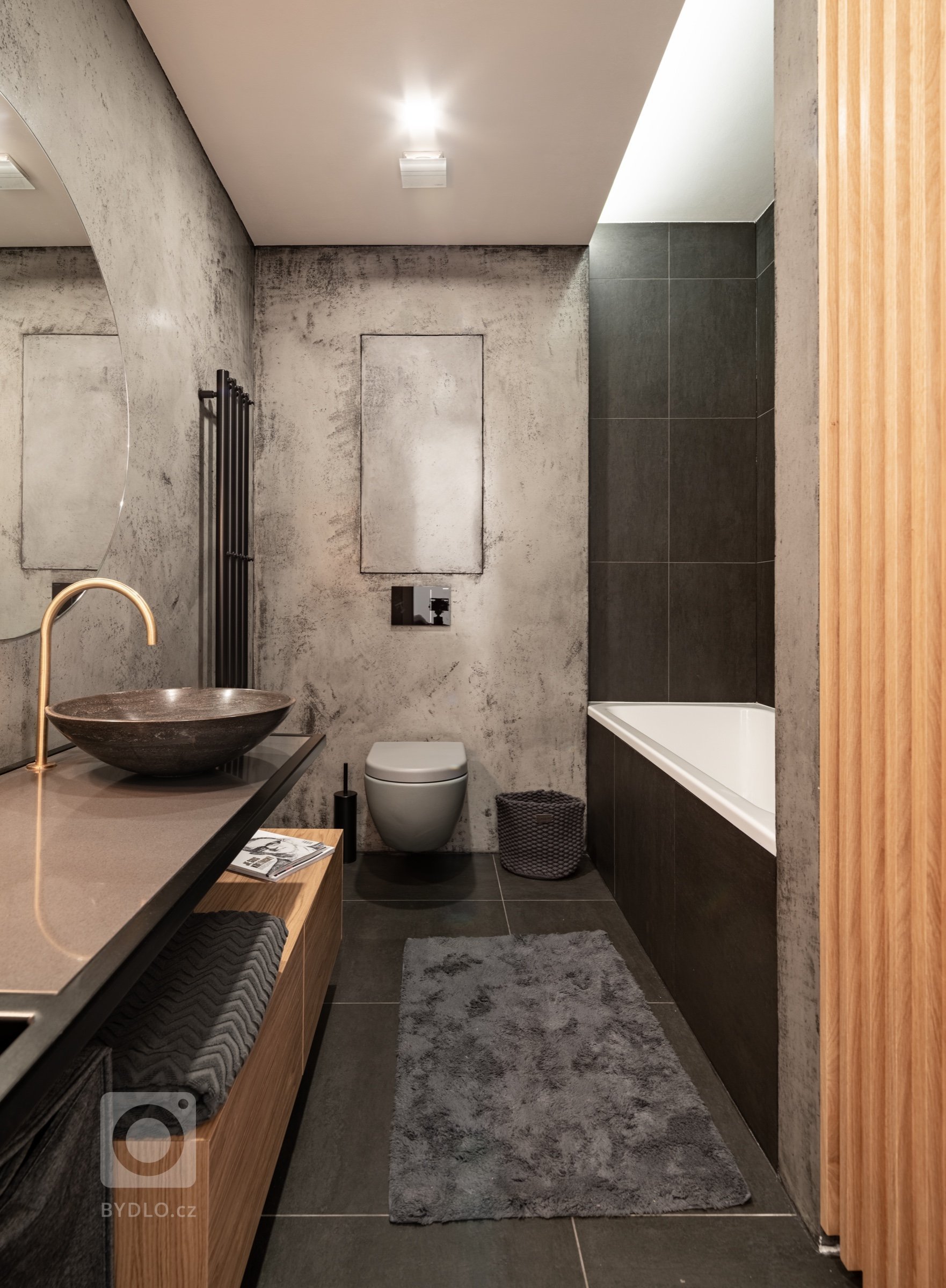 Sanita je použita šedá a je spíš upozaděna oproti kamenným umyvadlům a mosazným bateriím, které naopak vynikají a stávají se tak “šperky “ koupelny. 