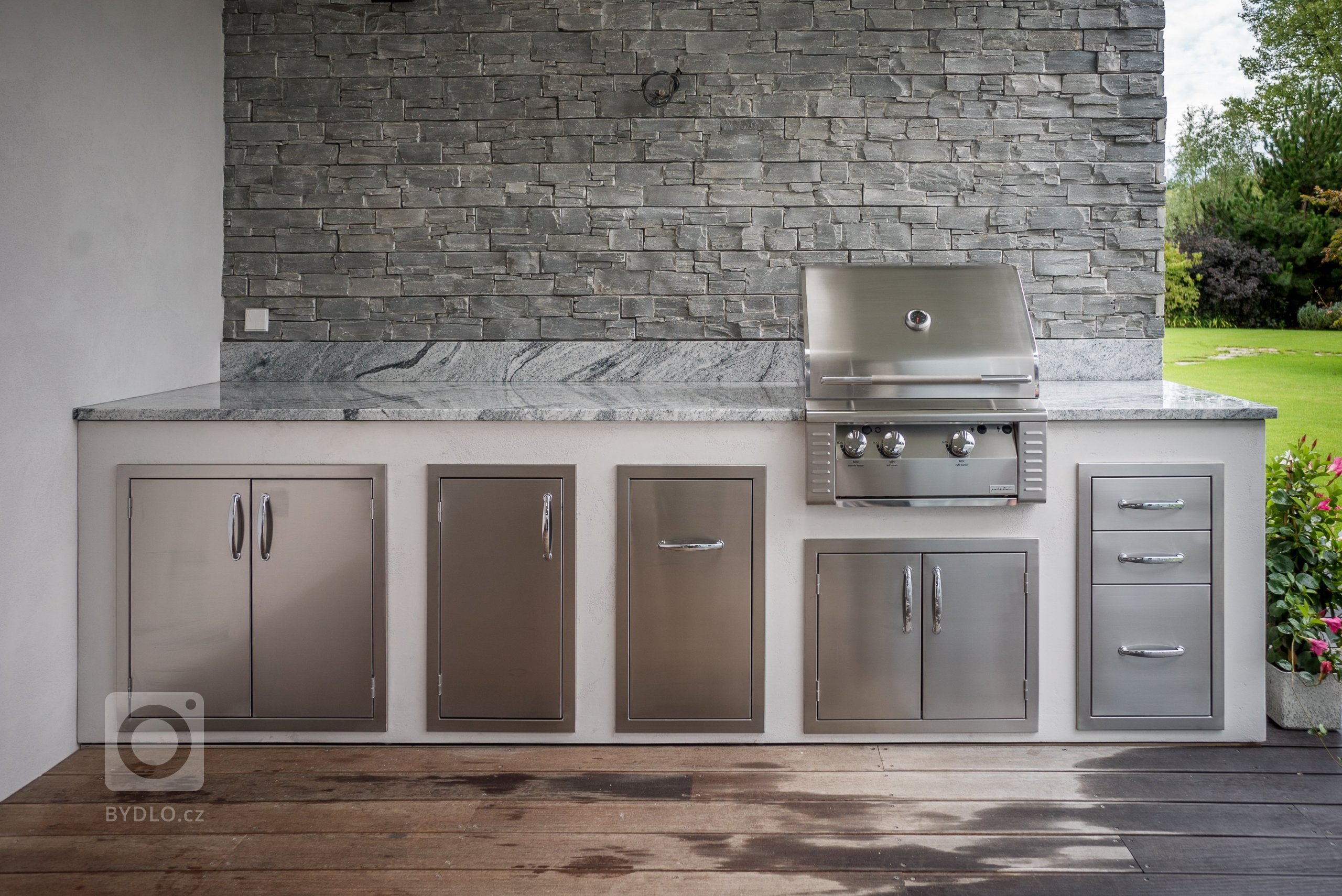 Jednoduchá kuchyňská linka na terase rodinného domu s 26ti palcovým grilem a úložnými prostory. Žulová deska v odstínu Viscont White a pohledové stěny v…