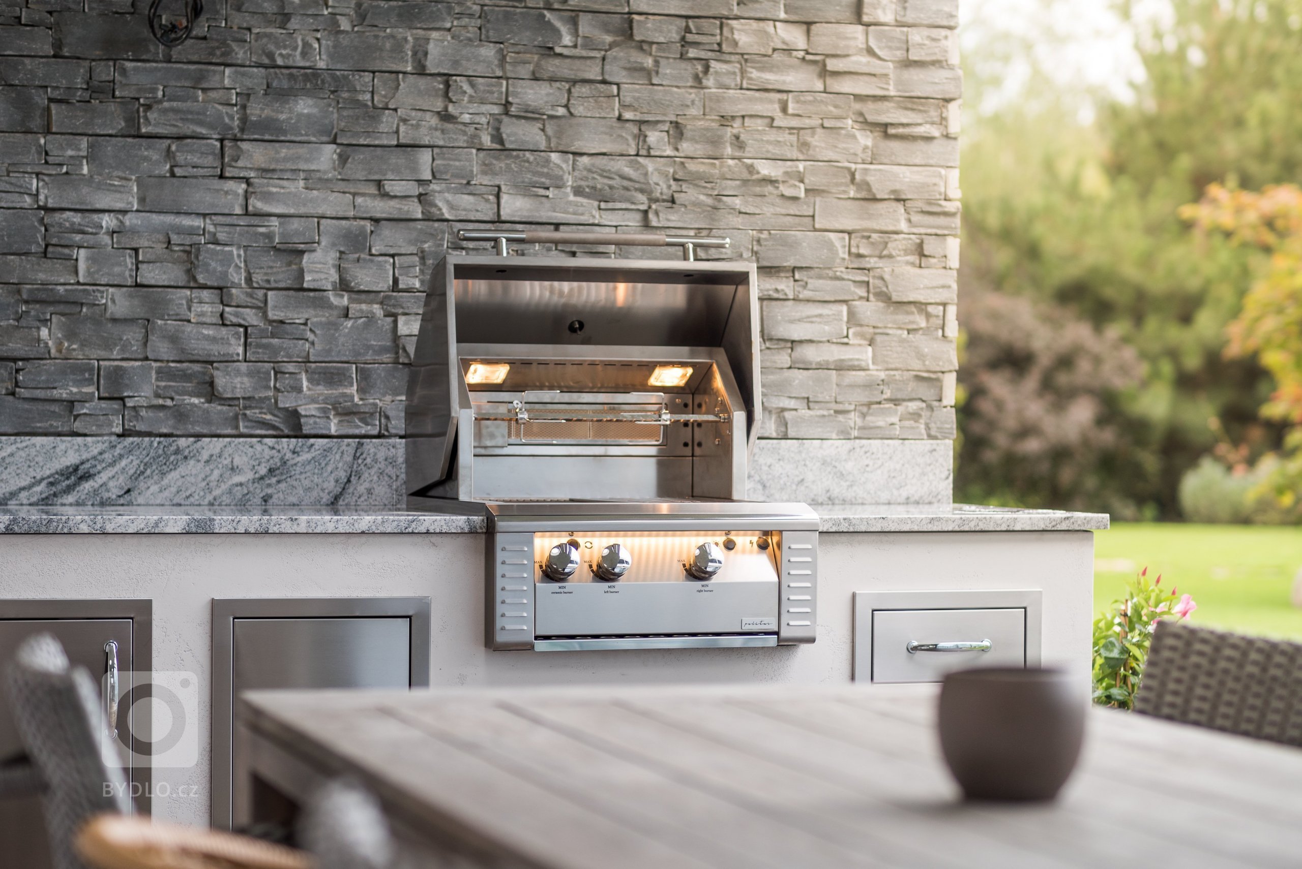 Jednoduchá kuchyňská linka na terase rodinného domu s 26ti palcovým grilem a úložnými prostory. Žulová deska v odstínu Viscont White a pohledové stěny v…