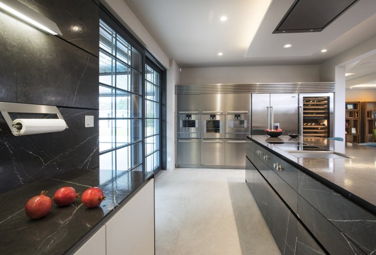 Kuchyň EGGERSMANN UNIQUE, rodinný dům. Provedení je masivní kámen Graphit Brown Leather na ostrůvku v&nbsp;kombinaci s Paso supermatt lotus white a broušeným…