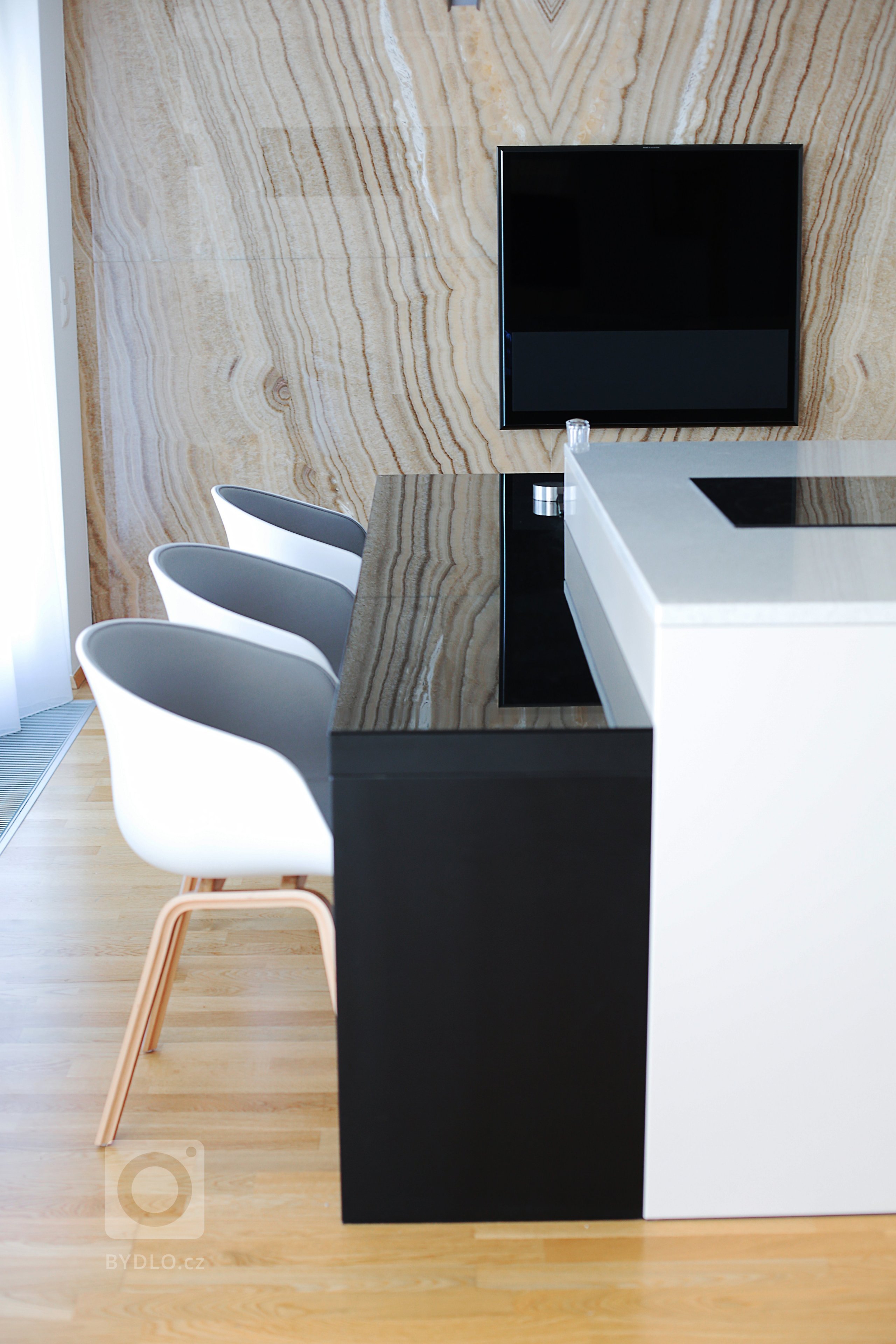 V jinak velkorysém bytě chybělo místo pro klasický jídelní stůl. Na velkém jídelním stole netrval ani investor, protože doma vaří minimálně. Vznikl tak černý lakovaný stůl na míru, který se stal součástí kuchyňského ostrůvku a nabízí standardně čtyři místa. Po rozložení až šest. Navíc krásně zrcadlí onyx na stěně.