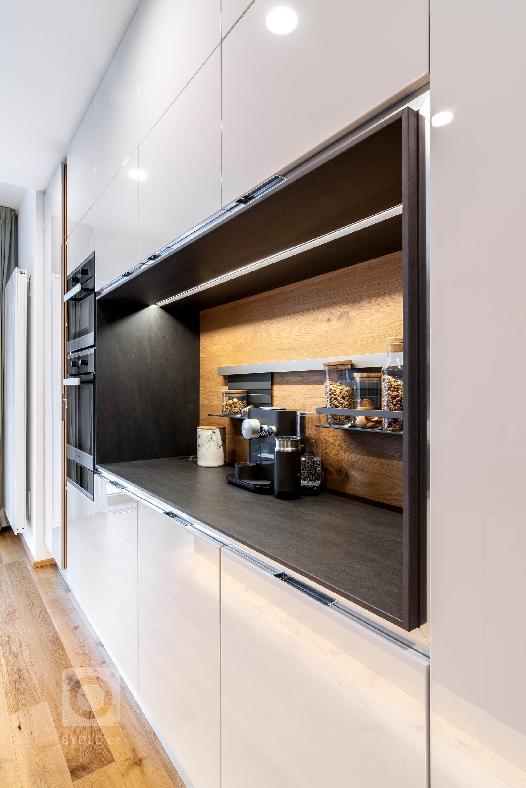 Kuchyň v lesklém laku Grey s velkoryse pojatým odkládacím prostorem, policemi a zástěnou z kartáčovaného dubu. Vysoká sestava, která využívá celou výšku…