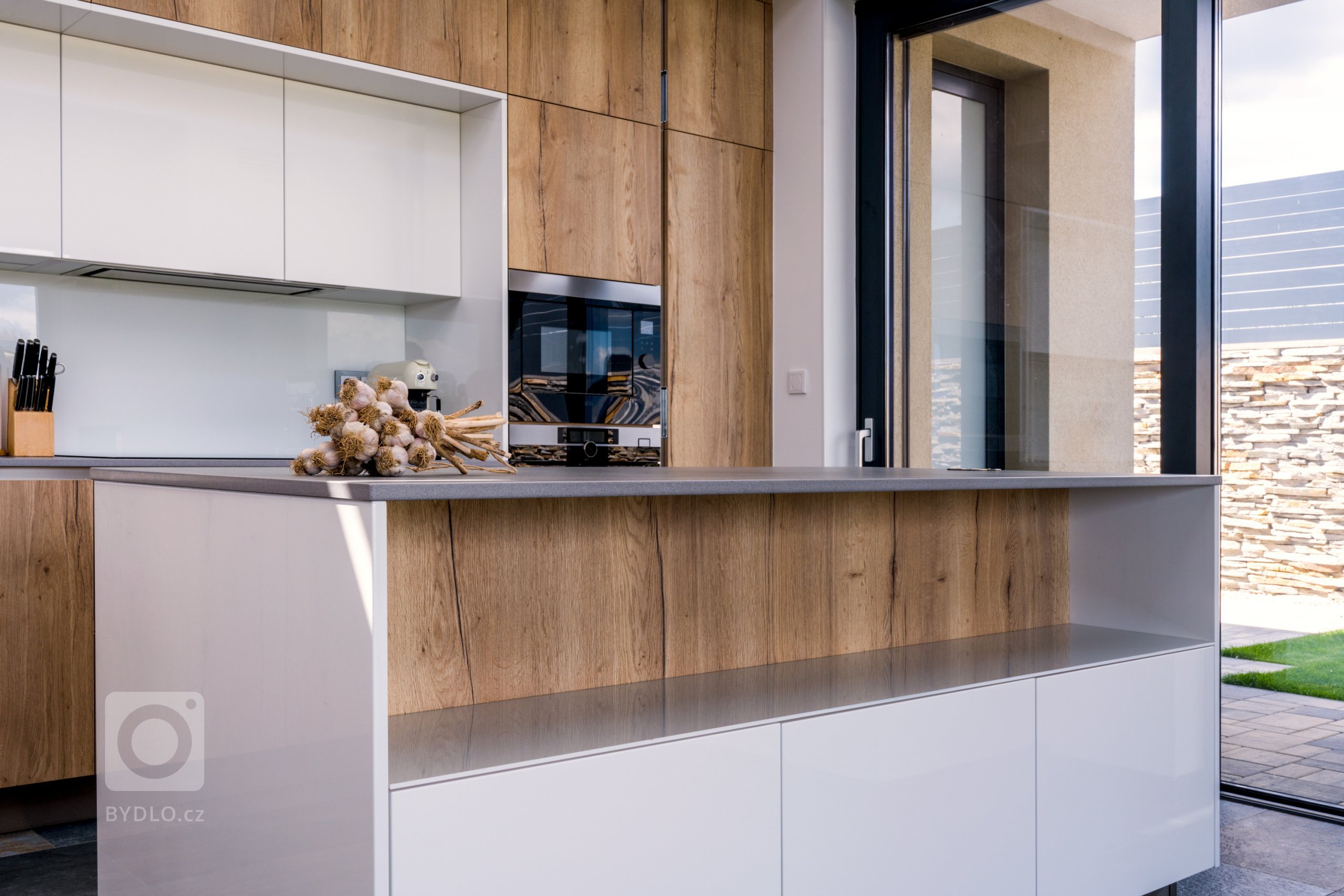 Kuchyňskou stěnu doplňuje, či spíše rozšiřuje také ostrůvek s šedou pracovní deskou v dekoru Dekton - Keon.