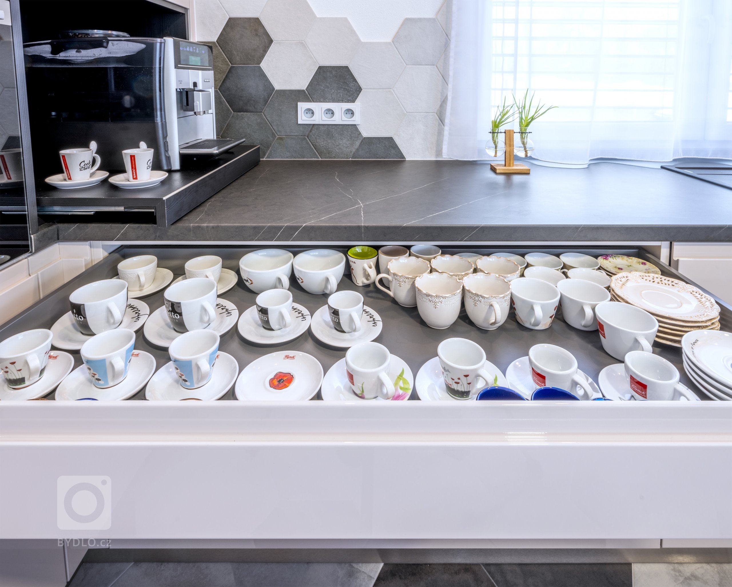 Za tajnou místností a vestavnou lednicí navazuje technologická stěna. Kromě trouby je zde i výsuvná nika s kávovarem. Hned pod ním mají majitelé zásuvku s hrníčky a šálky. Když je chuť na dobrou kávu, nic jim nestojí v cestě. 