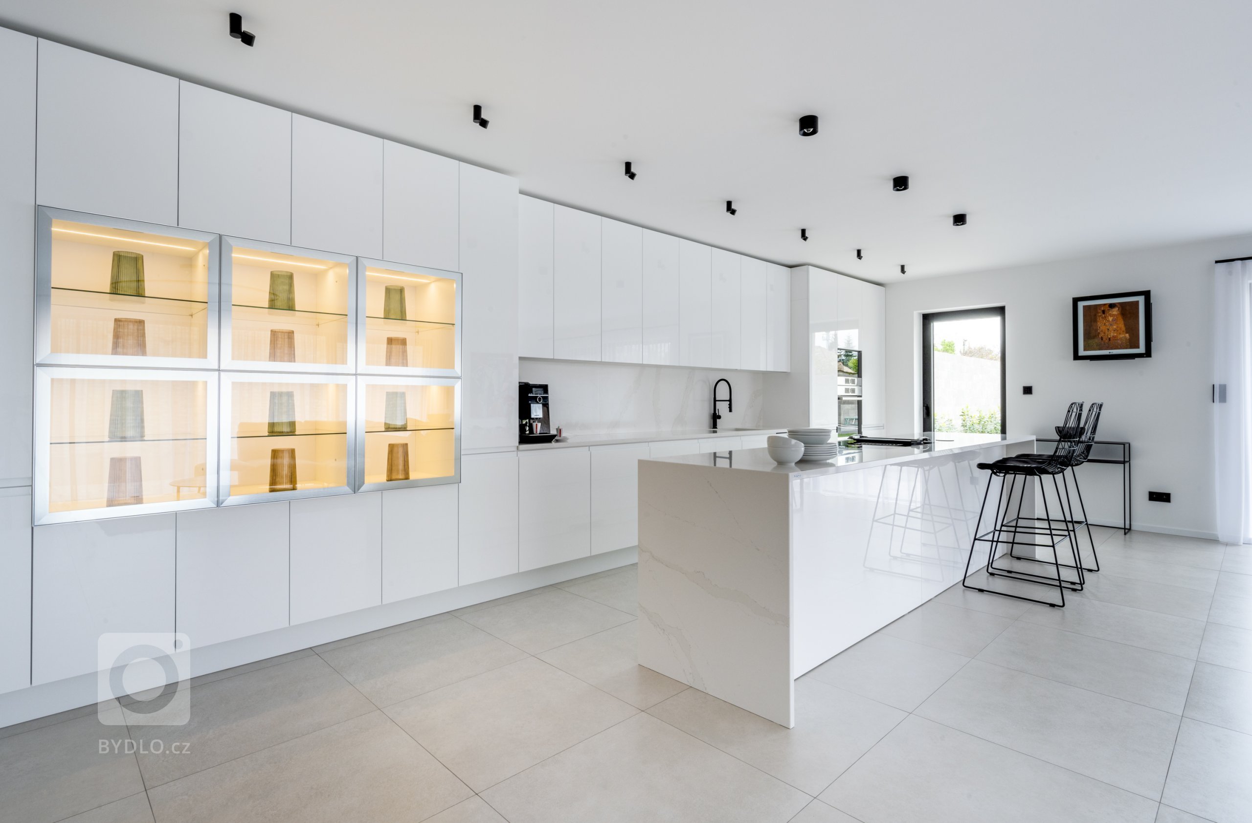 Specialitou sestavy, něčím, co originálně vybočuje z šablon, je prosklená vitrína v levé části vysokých skříní. Prosvětluje už tak jasný prostor, a díky vnitřnímu podsvícení mu dodává až magickou hladivost.