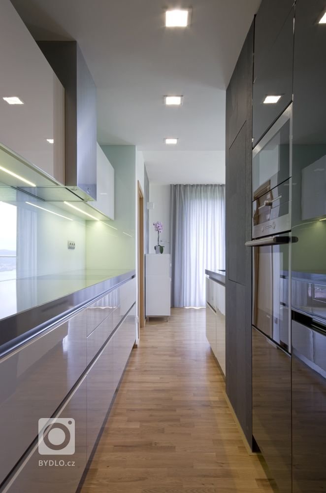 kuchyňská linka v odstínech bílé a šedé, v ušlechtilých materiálech jako je bílý lak, umělý kámen a skleněný obklad