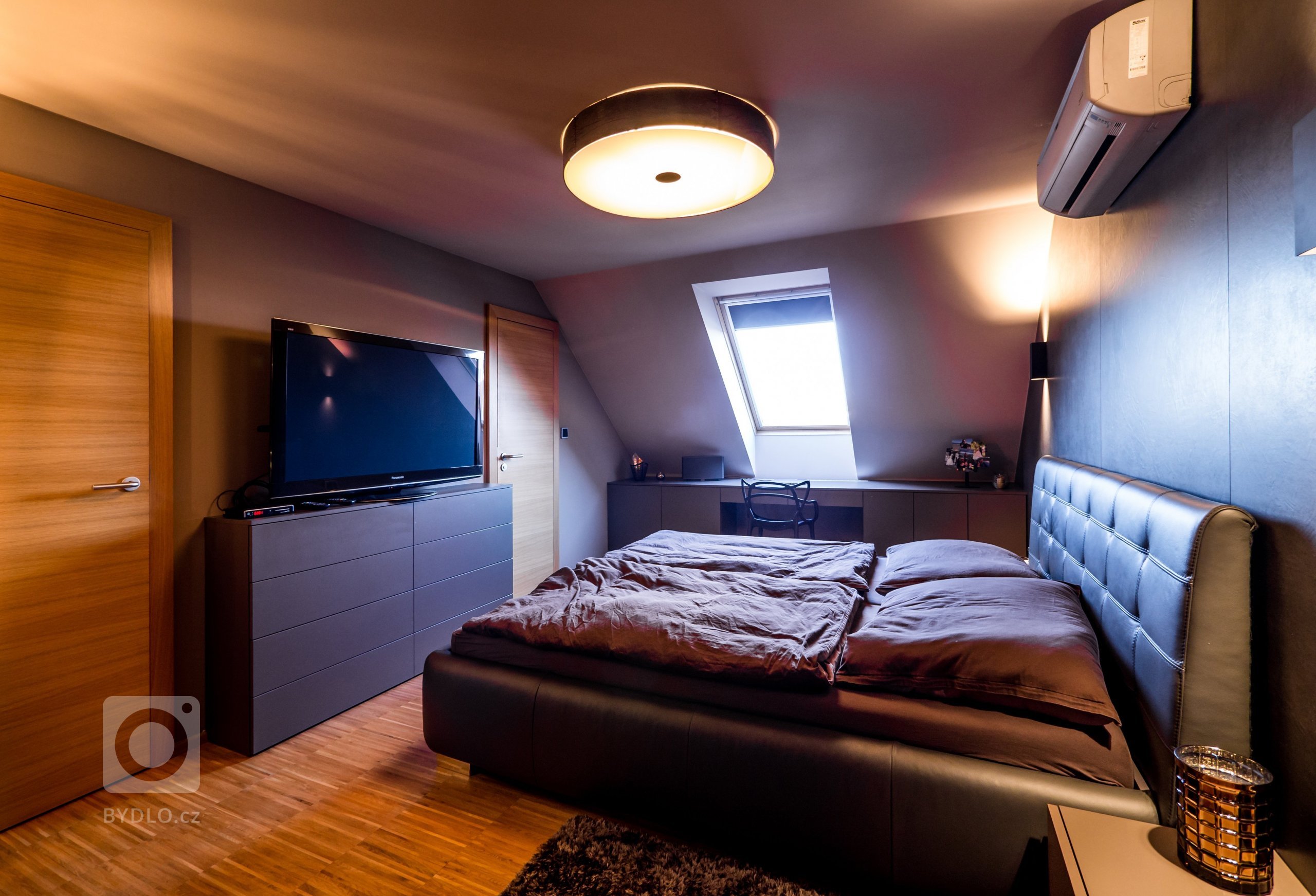 Ložnice je řešena netradičně v tmavých barvách a stěna za postelí je opět opatřena velkoformátovým obkladem v nadstandardní velikosti kachlí.