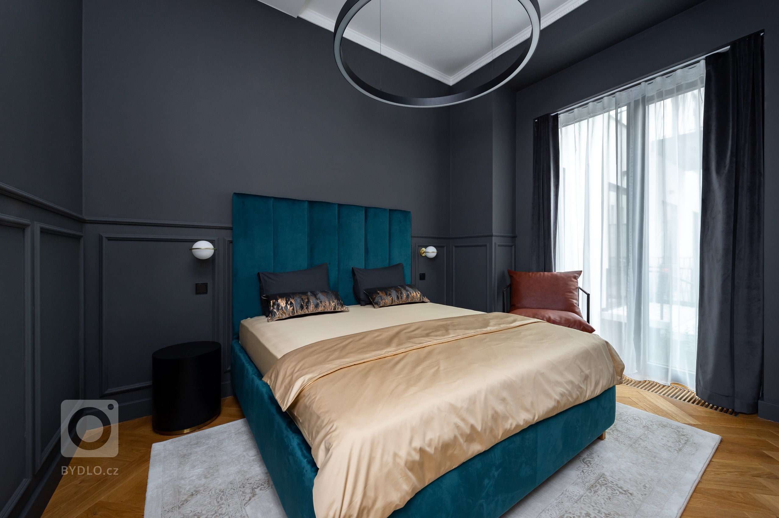 Ložnice s čalouněnou postelí ze zeleného sametu vyrobenou na míru. Atypická výška čela postele je 170 cm. Na stěnách jsou okrasné lišty a celá místnost je vymalována do antracitové barvy. 