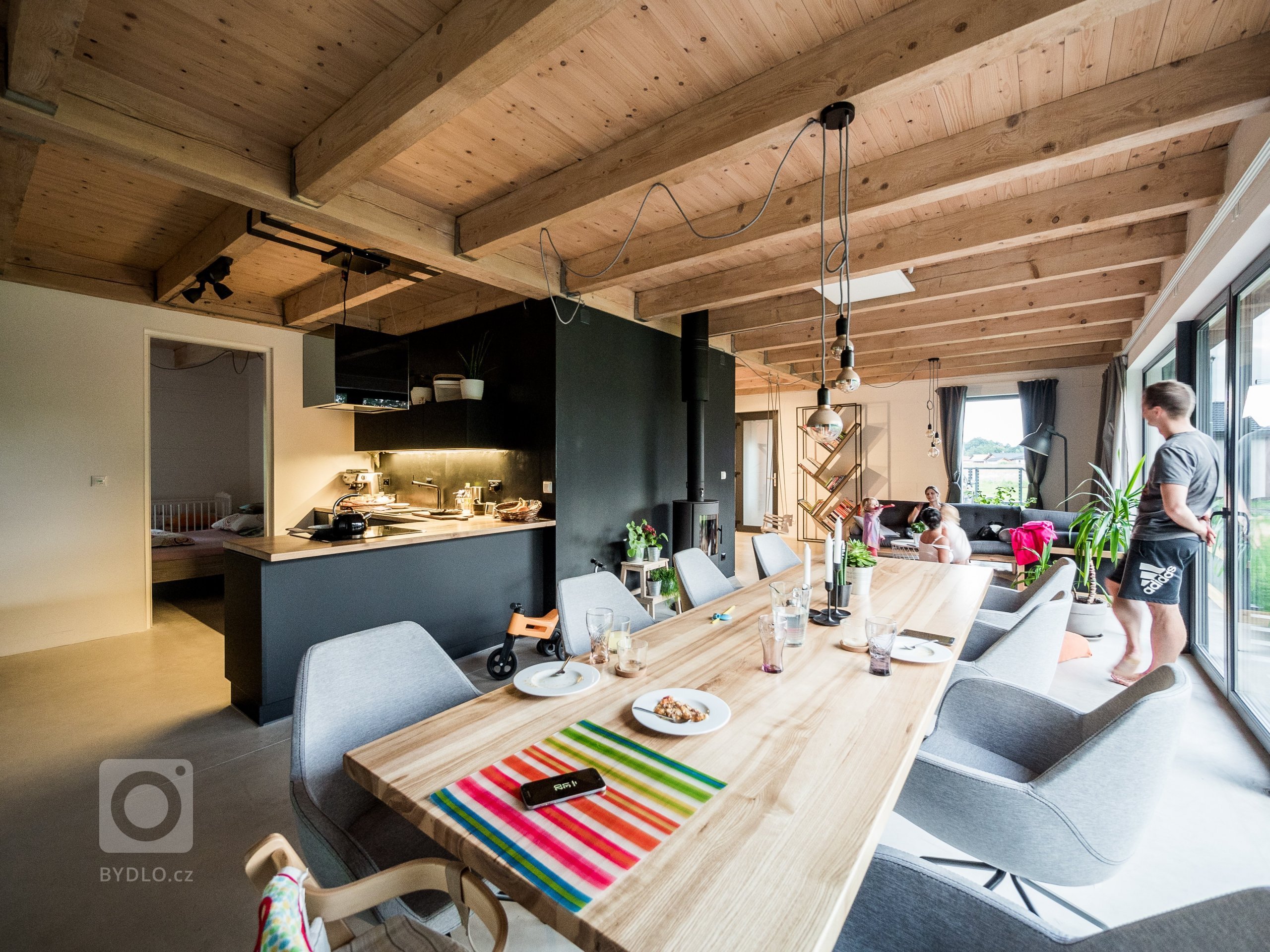 Obytný prostor ZEN HOME, osvědčená kombinace betonové podlahy, dřevěného stropu, černé stěrky i kuchyně a velkého prosklení.